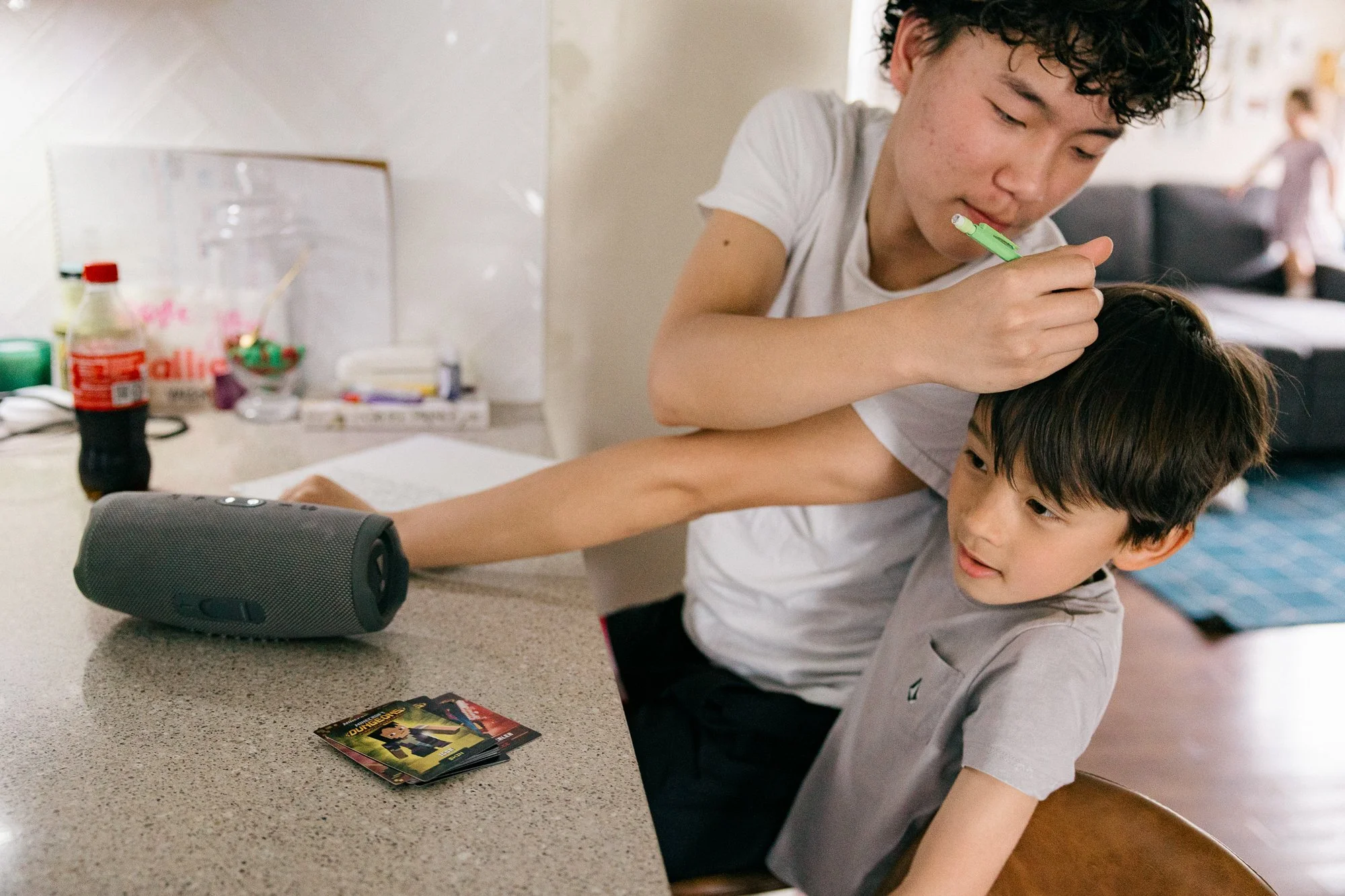 Teenage boy casually fixing his younger cousin's hair at the kitchen counter, candid moment during a documentary family photography session by Mel Usry Photography, Northern Virginia