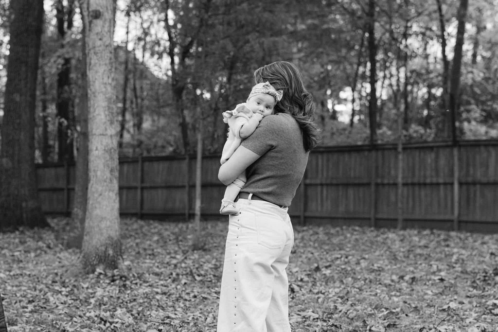 Mother holding her baby during a documentary family photography session in a backyard in Sterling, Virginia.