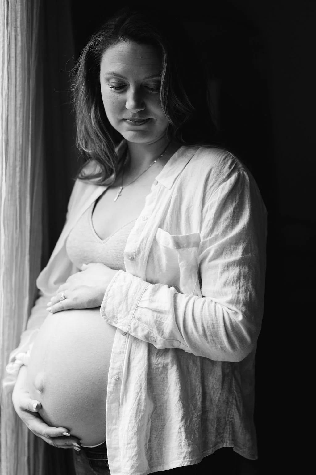  Black and white documentary maternity portrait of an expectant mother standing by a window during an in-home maternity session in Sterling, Virginia 