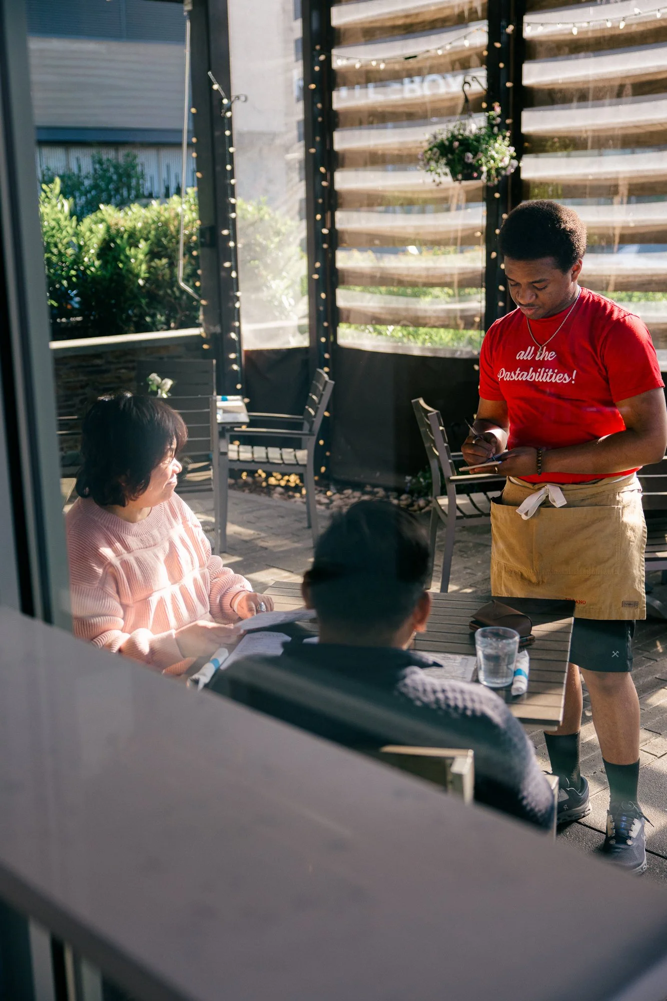 A server takes an order from two guests on the outdoor patio at Urbano Modern Italian restaurant, captured candidly during a documentary brand story session by Mel Usry Photography in Sterling, Virginia.