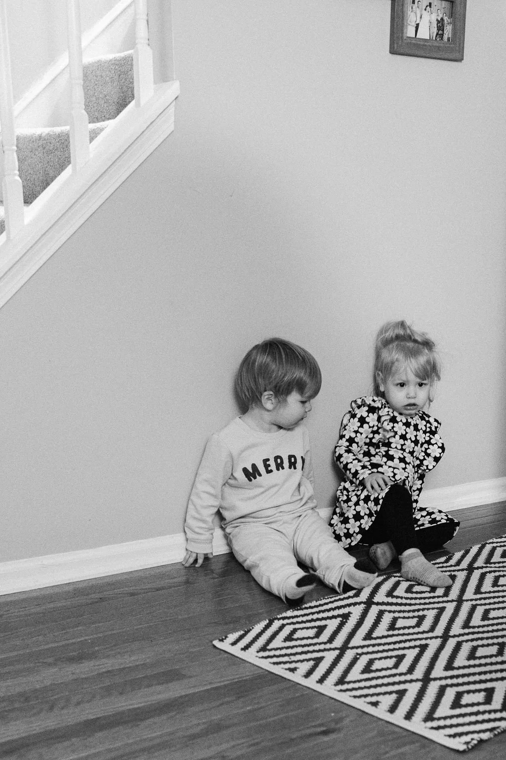 Two young children sit quietly together against the wall of their home in Sterling, Virginia, photographed using a documentary family photography approach.