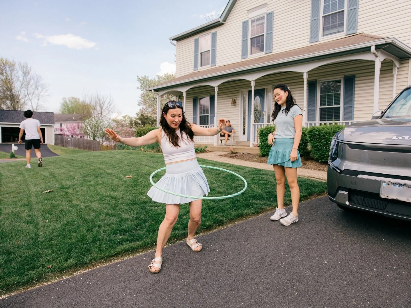Mom hula hooping in the front yard with her teenage daughter watching, candid family moment captured by documentary family photographer Mel Usry Photography, Northern Virginia