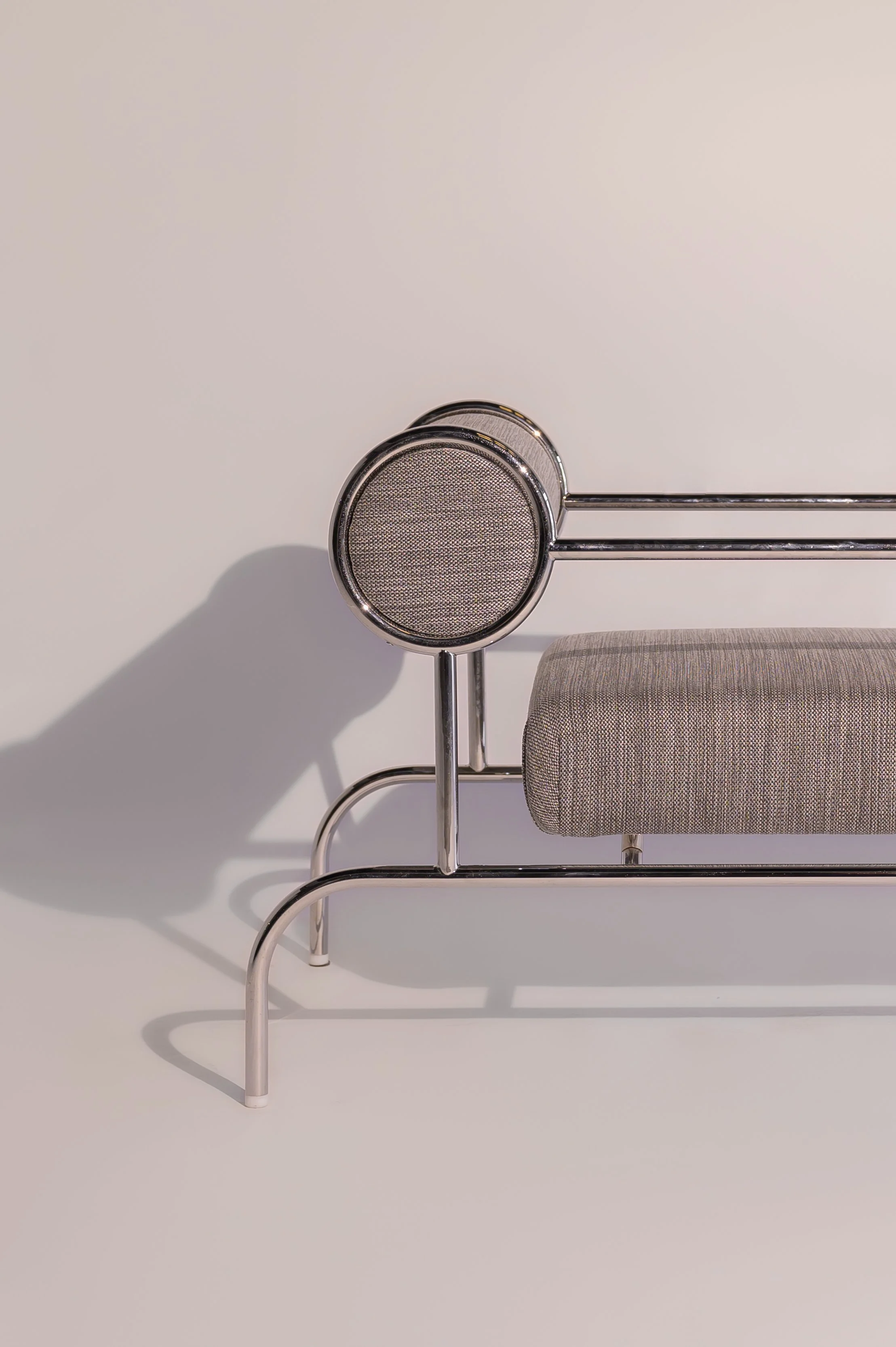Modern metal bench with a cushioned seat and a round, mesh-backed headrest, set against a plain white background, casting a shadow.