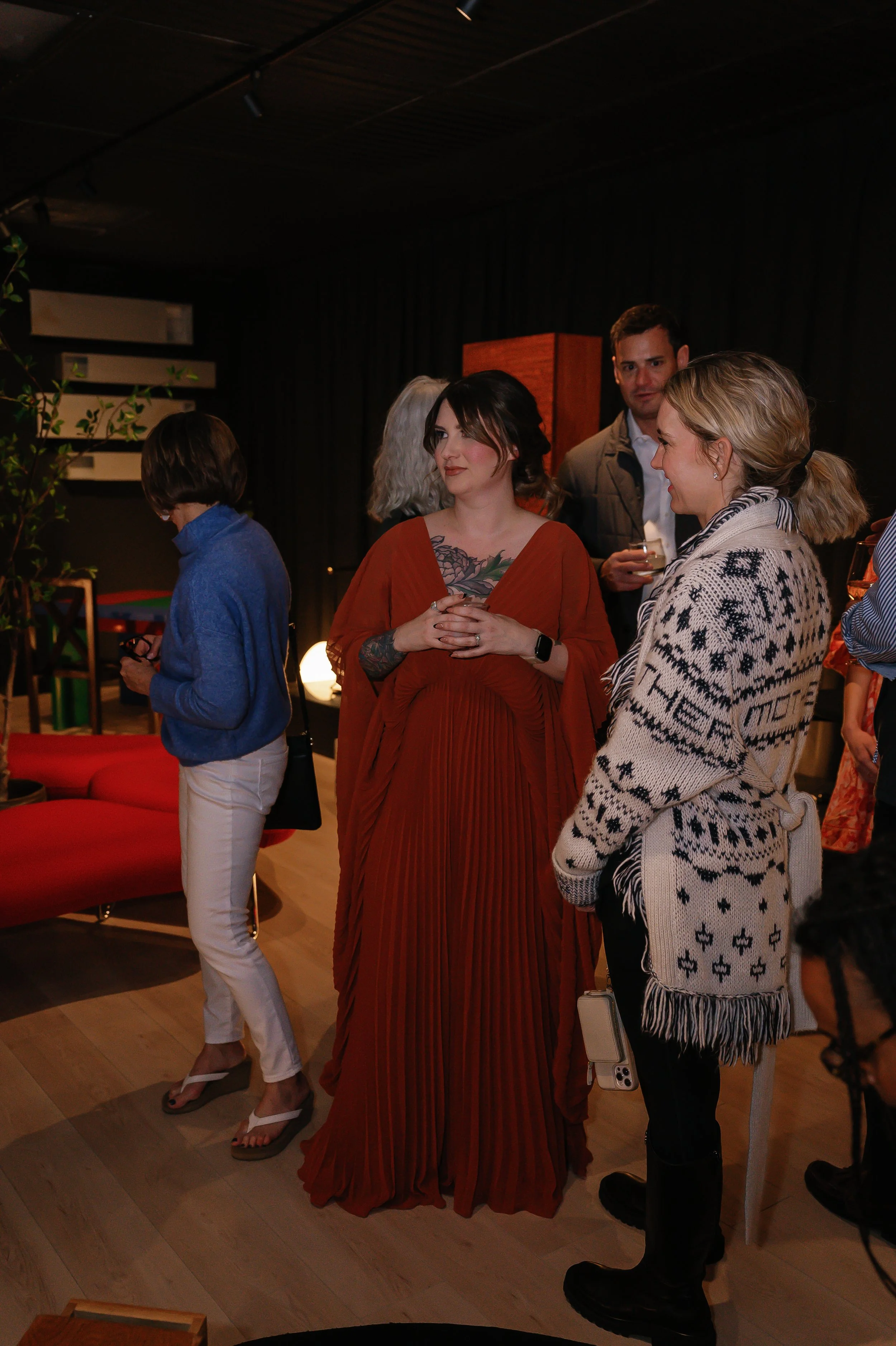 Group of people at a social gathering or party, talking and holding drinks indoors, with a mix of casual and formal attire.