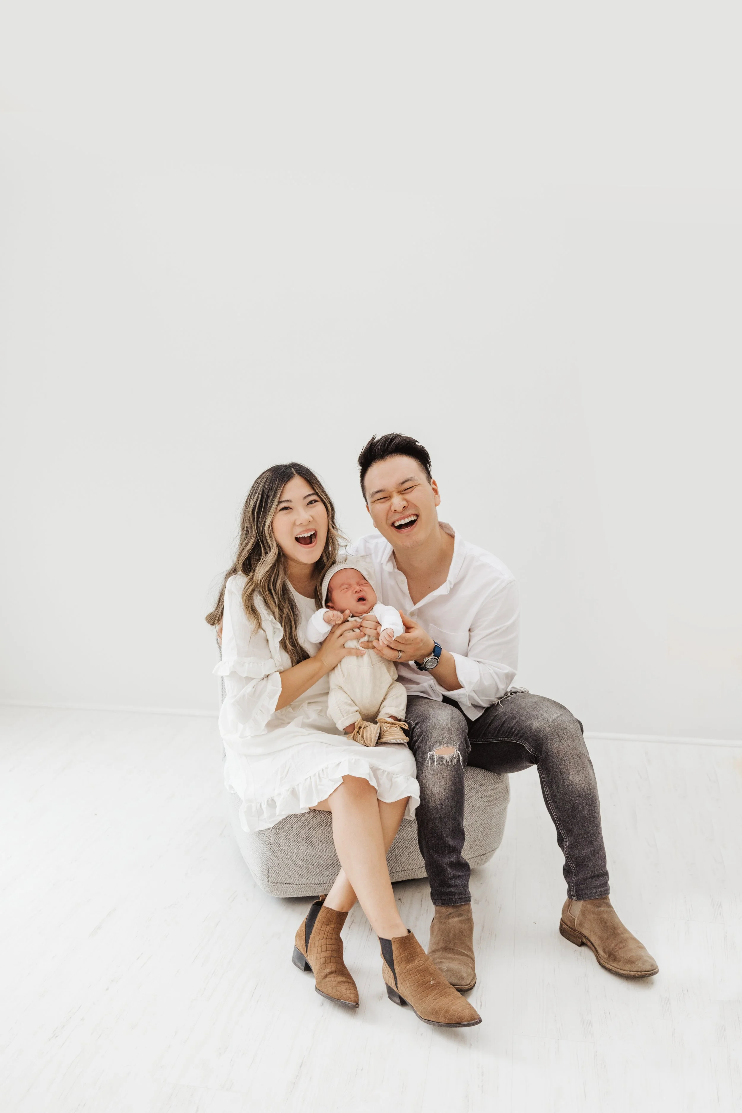 Happy family with infant sitting on a stool in a white room.