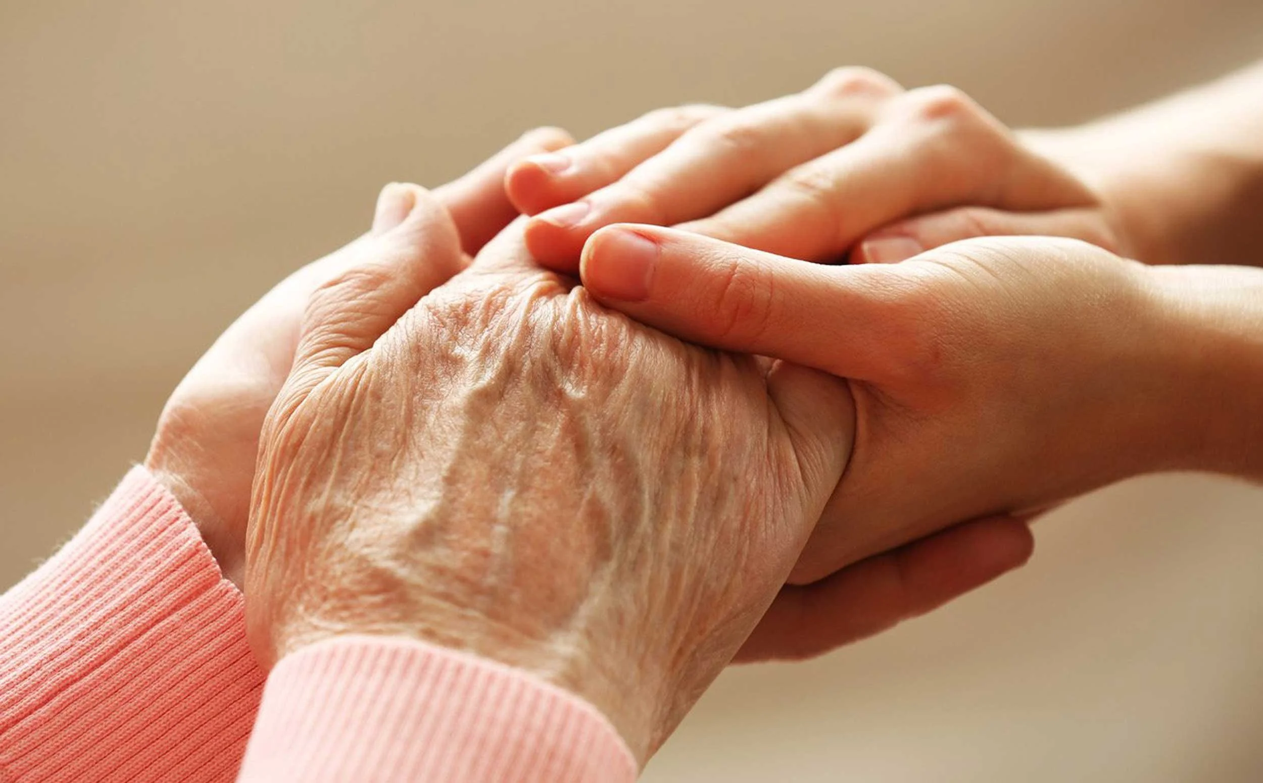 Close-up of a younger person's hand gently holding an elderly person's hand.