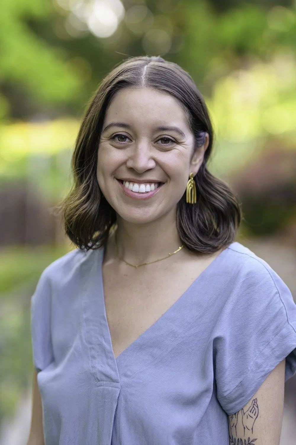 Jacqueline Esquer, California anxiety and trauma therapist in a light blue top photographed outdoors with soft greenery in the background.