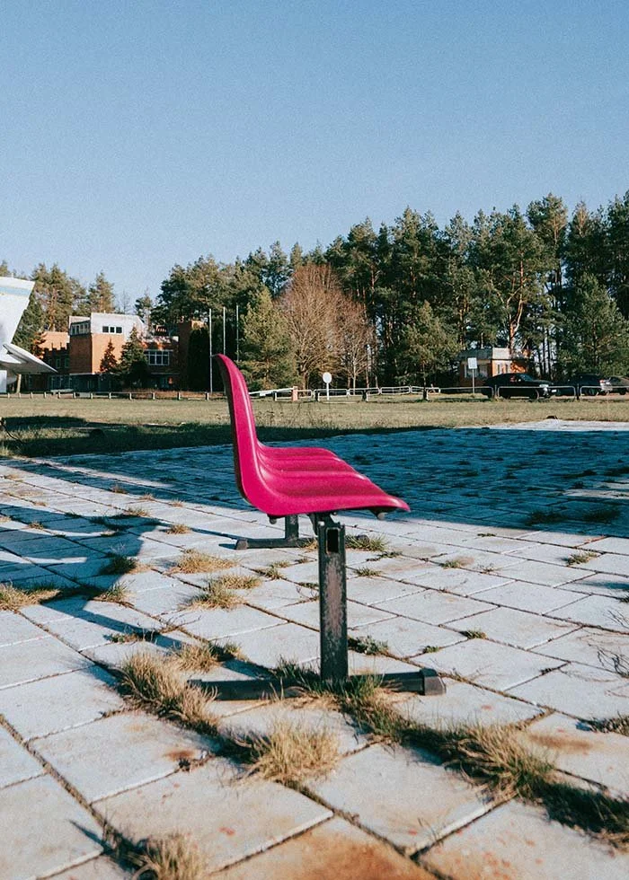 Bright pink chair mounted outdoors on a paved path with grass, trees, and blue sky in the background in California