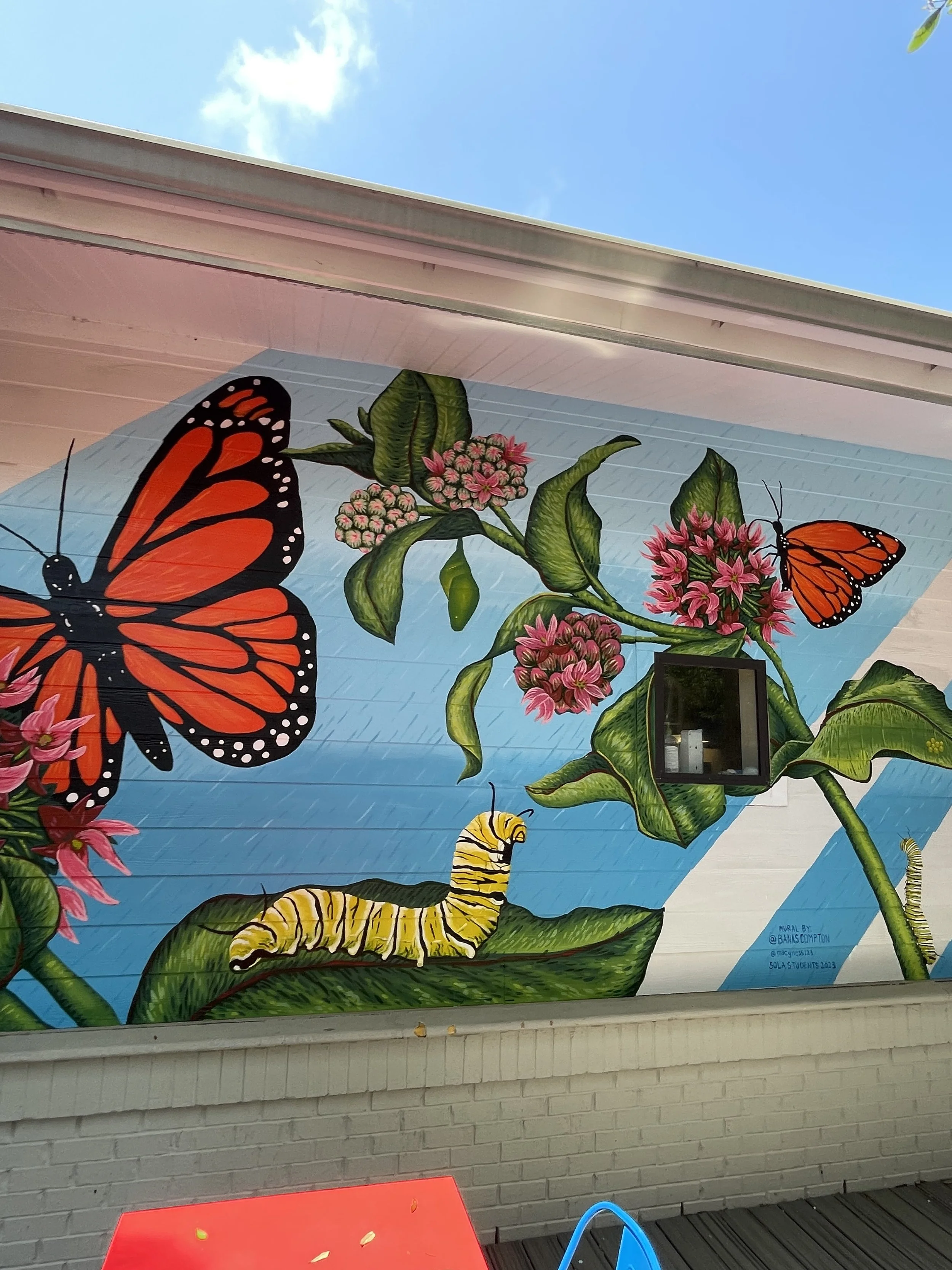 Educational mural by Banks Compton at the School of Liberal Arts in Pensacola, Florida, illustrating monarch butterflies, milkweed, flowers, and the monarch life cycle.
