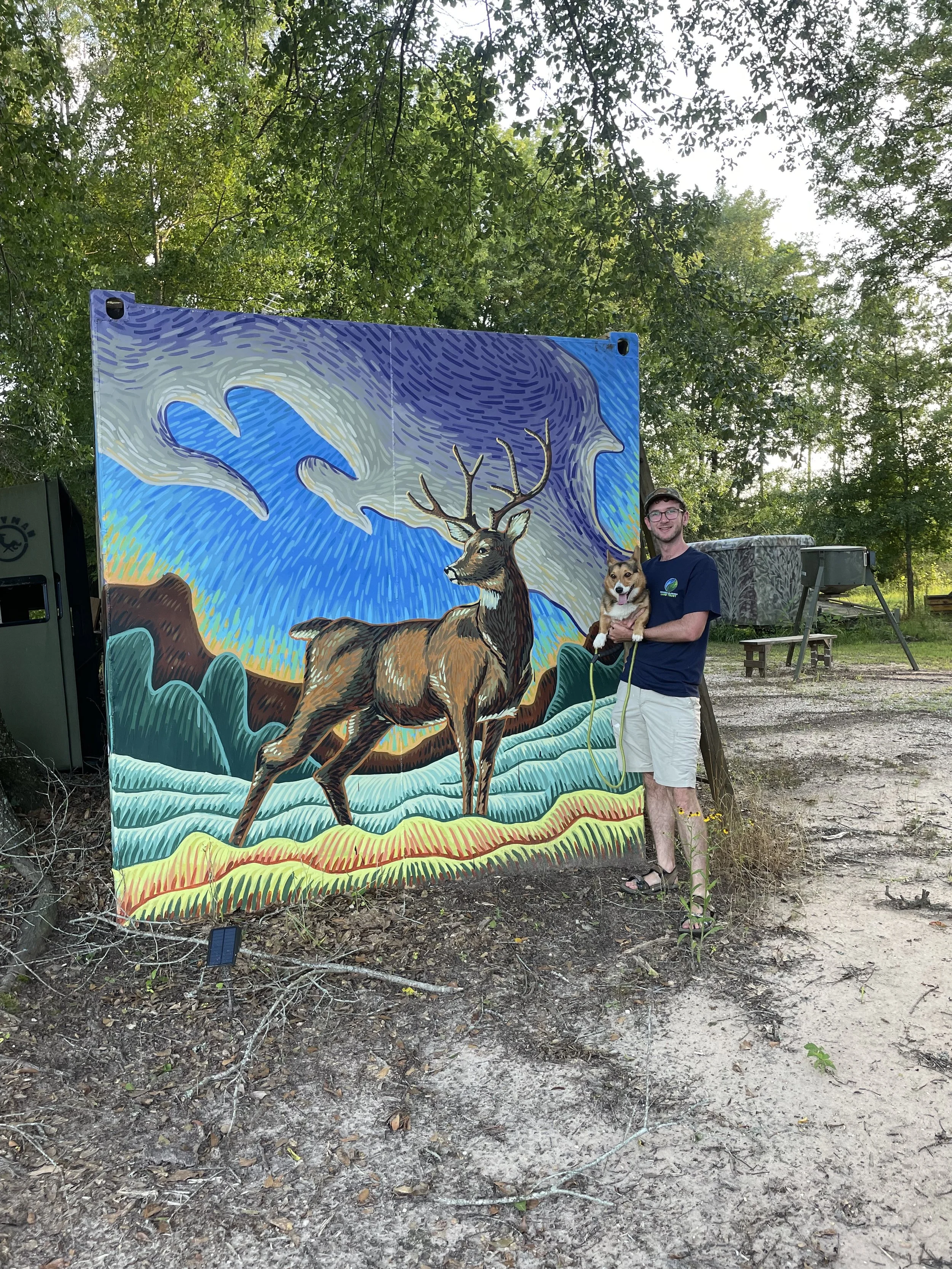 Banks Compton with a colorful wildlife mural at a hunting camp near Demopolis, Alabama, featuring a white-tailed buck in a rural landscape.