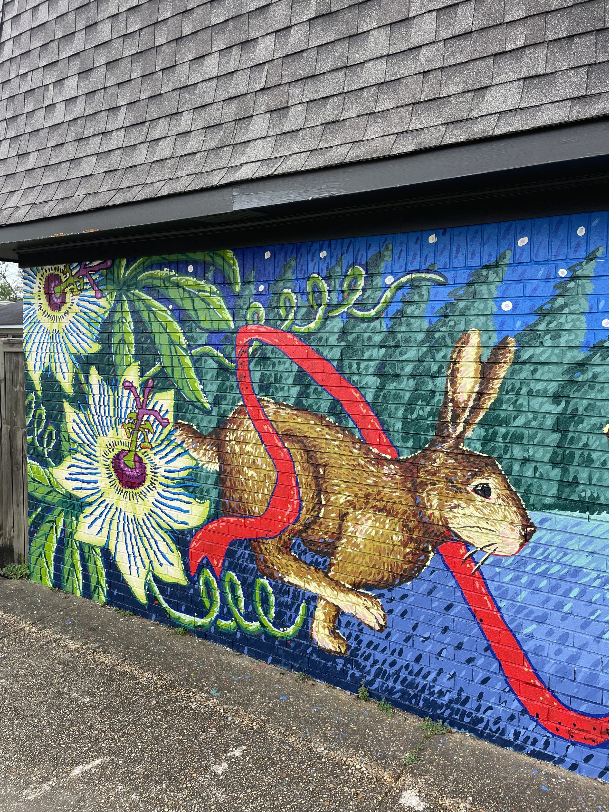 A colorful mural of a rat surrounded by plants and flowers painted on a brick wall in an outdoor setting.