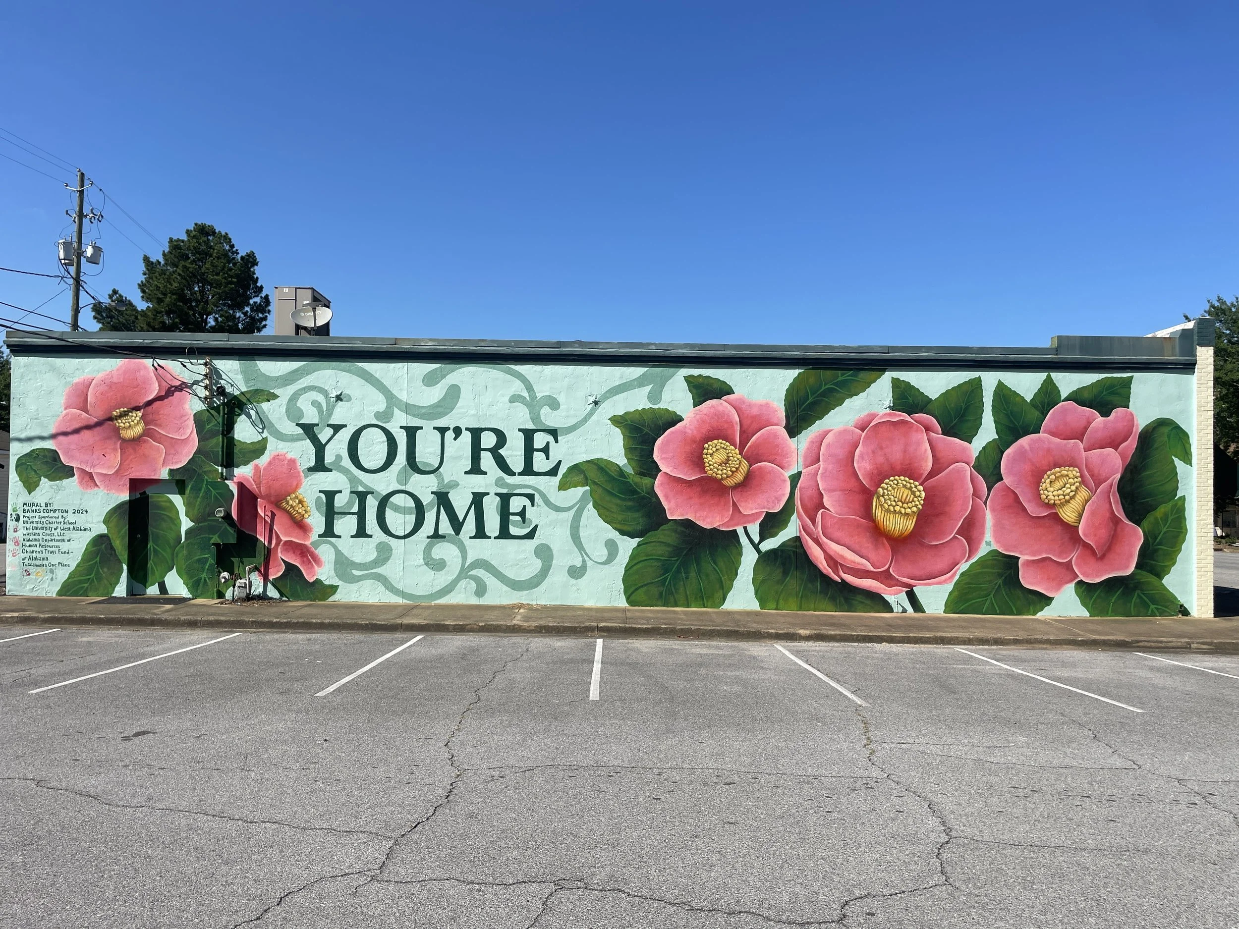 You're Home community mural by Banks Compton in Livingston, Alabama, featuring large pink camellias and local student contributions.
