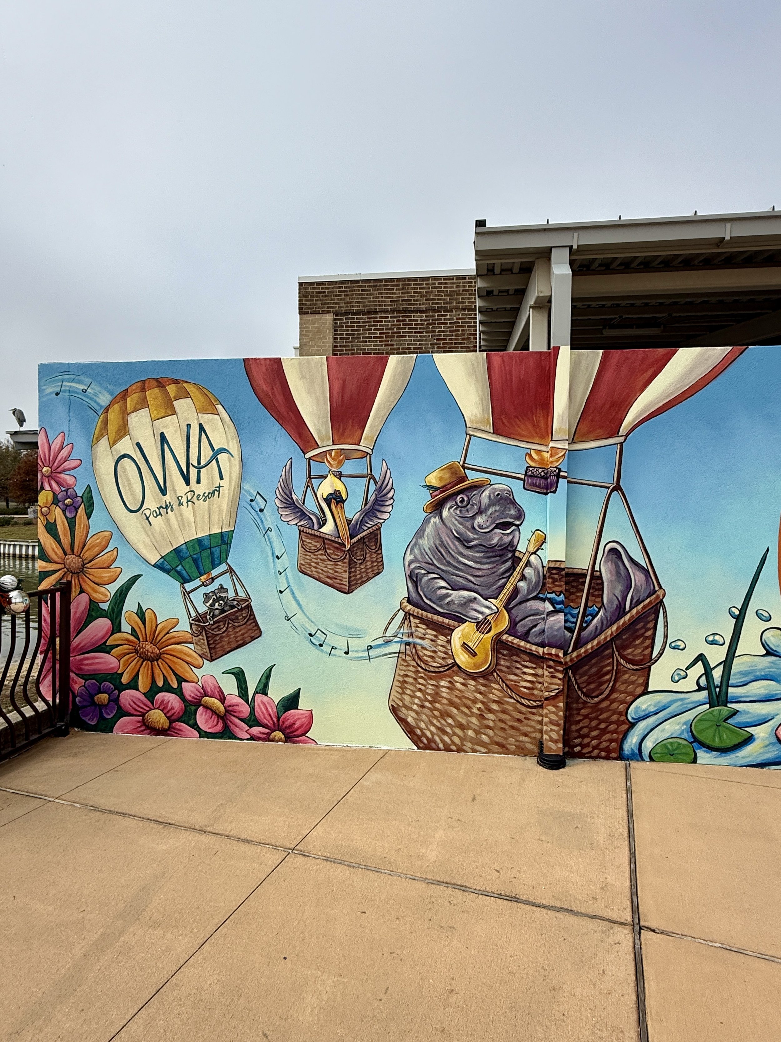 Colorful mural featuring a hot air balloon with the text "OVA Party & Resort," a hippo playing a guitar in a hot air balloon basket, and various flowers and water lilies.