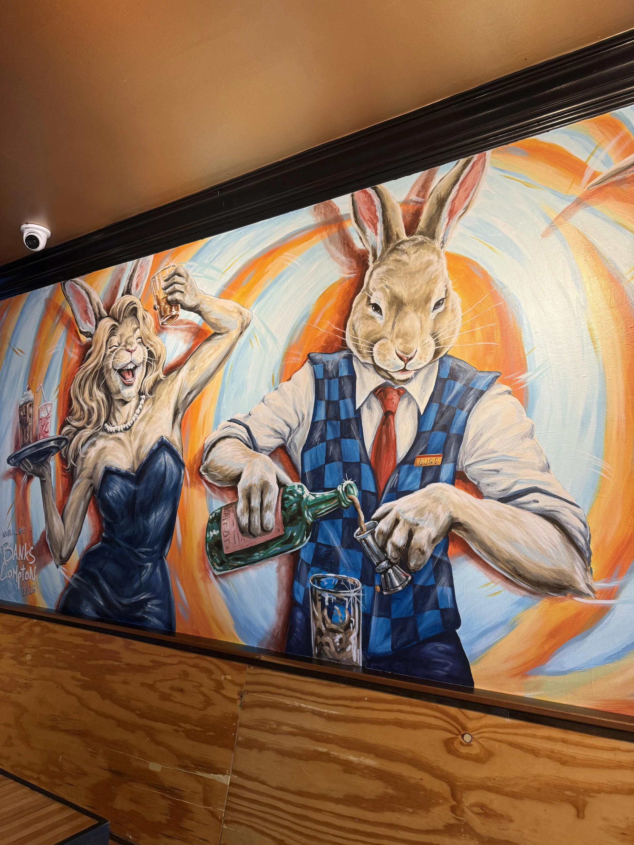 Rabbit Hole mural by Banks Compton in Tuscaloosa featuring whimsical rabbit bartenders serving drinks against a colorful background.