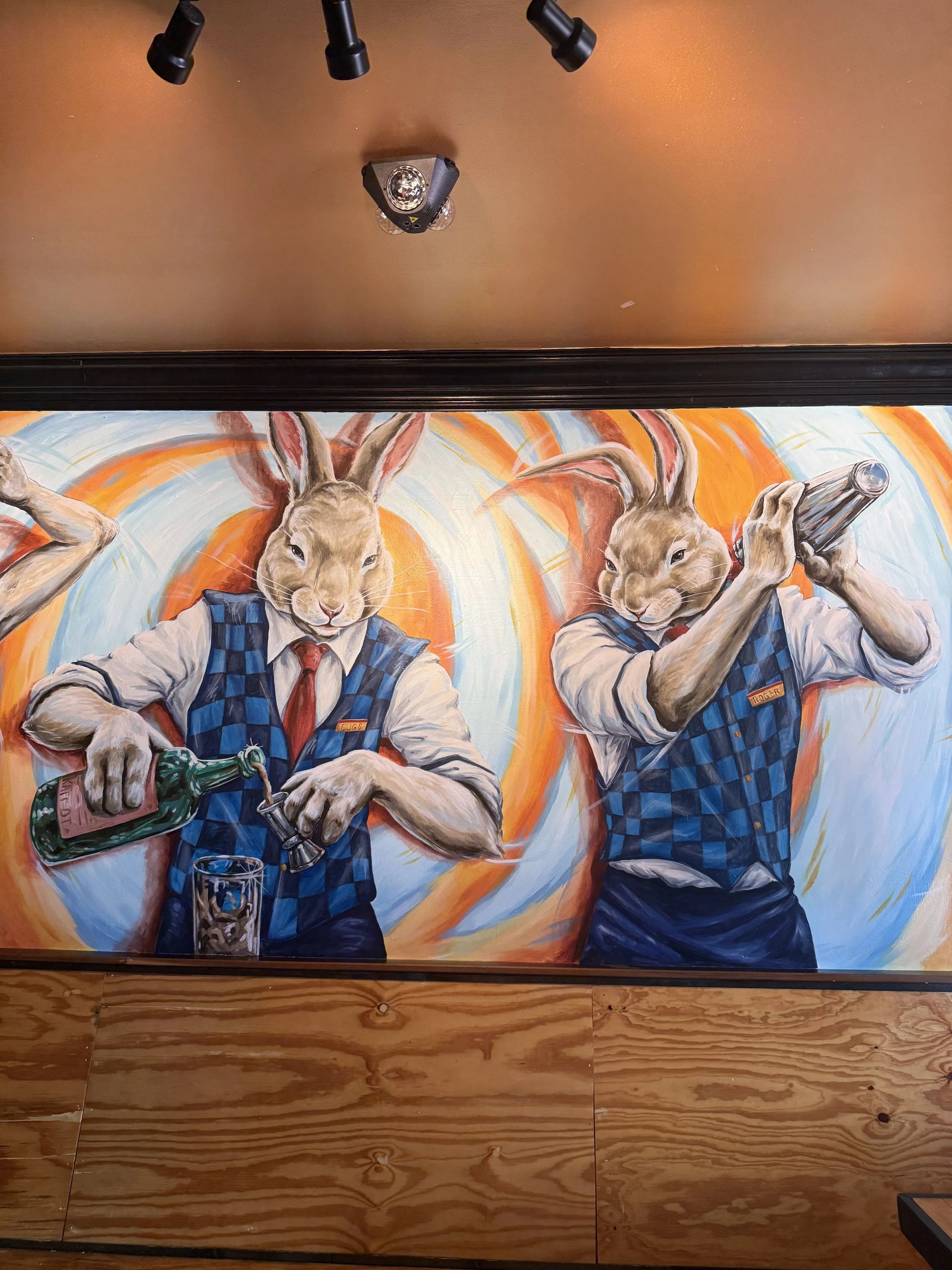 Wall art featuring two rabbits dressed in blue vests and red ties, with human-like arms, one pouring a drink and the other holding a glass, set against a colorful background.