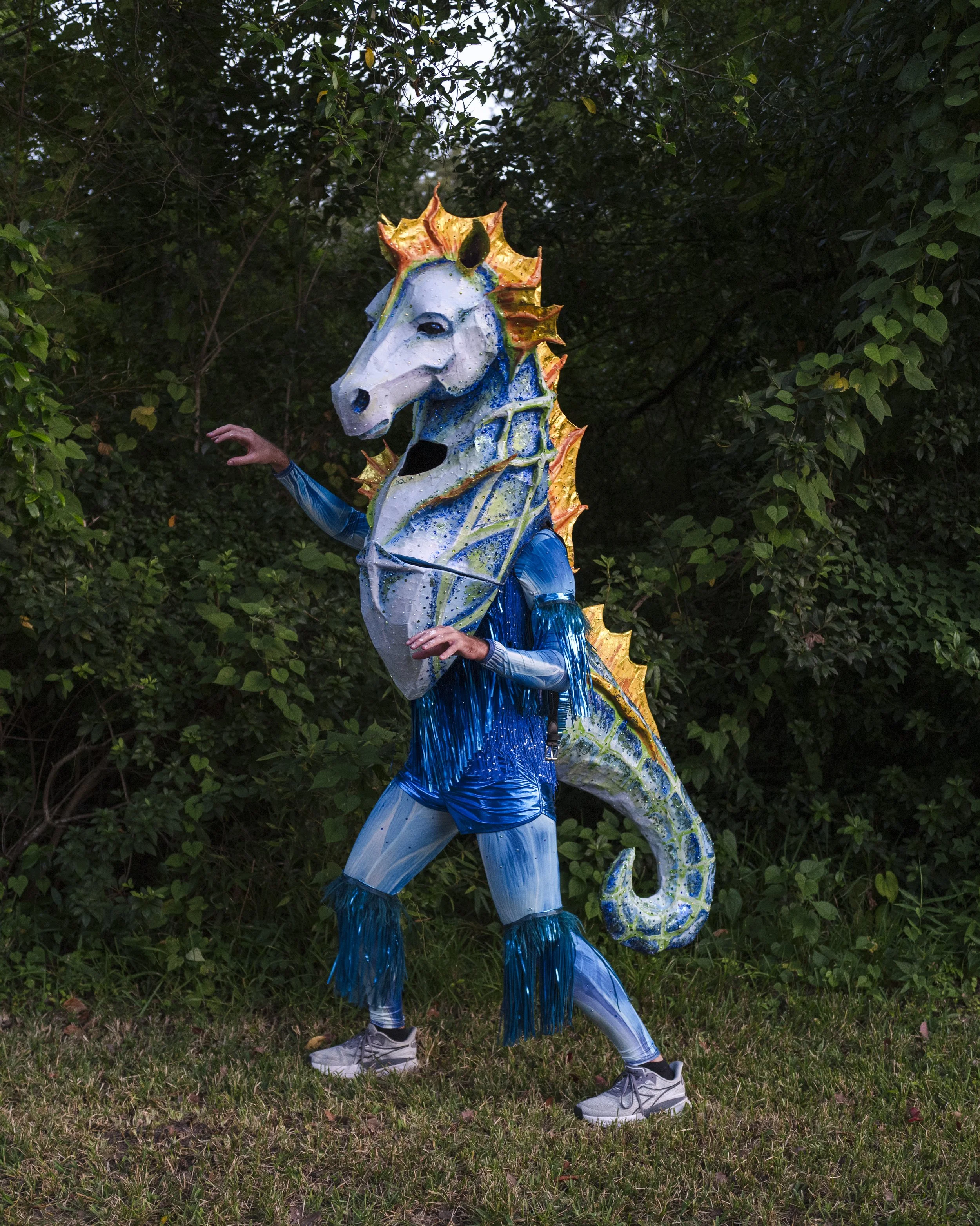 Wearable papier-mâché seahorse sculpture by Banks Compton featuring a blue and green body, orange fins, rhinestones, and shimmering fringe.
