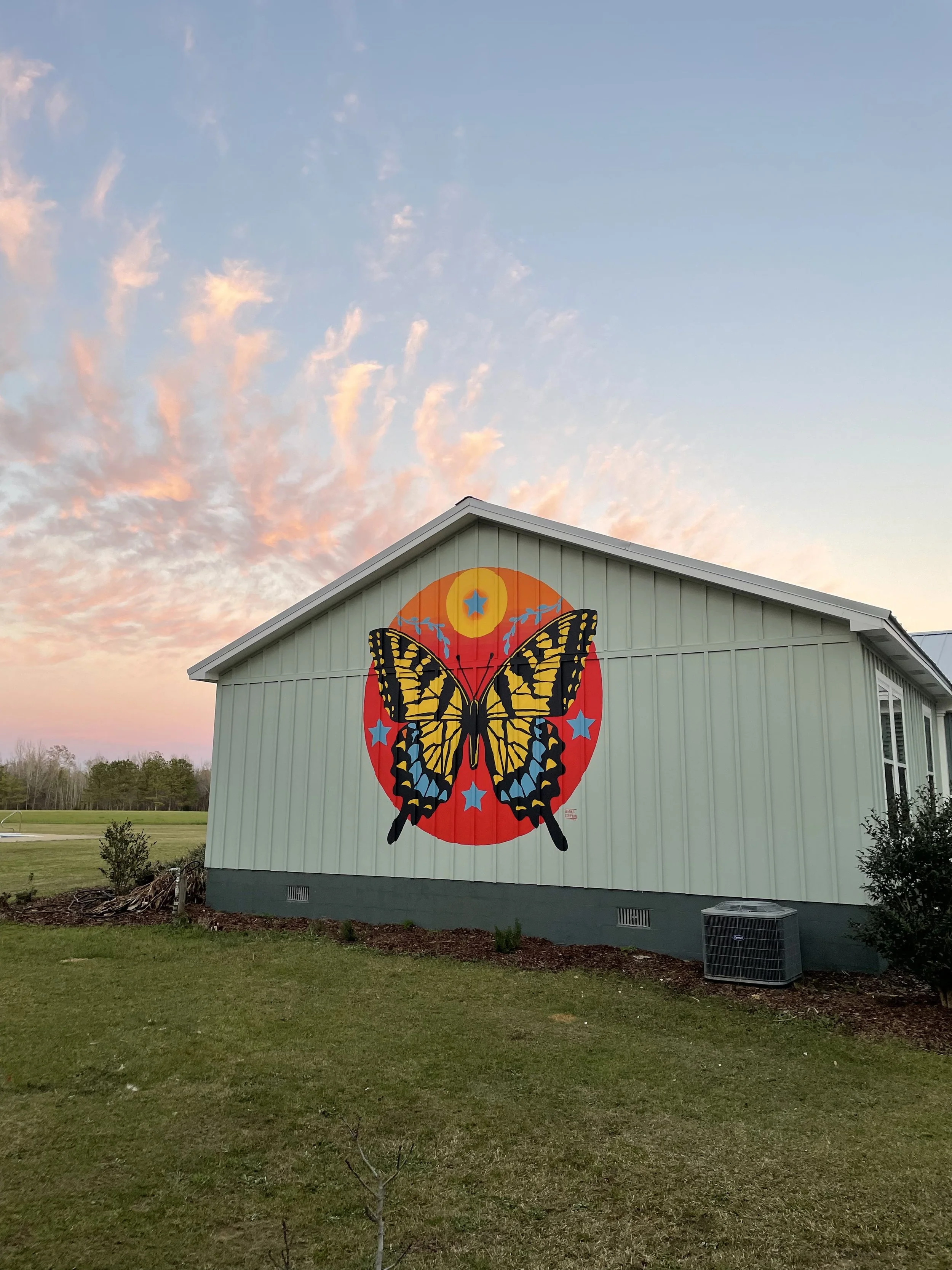 Tiger swallowtail butterfly mural by Banks Compton on a home near Demopolis, Alabama, featuring a large butterfly, four blue compass stars, and a red-orange sun.