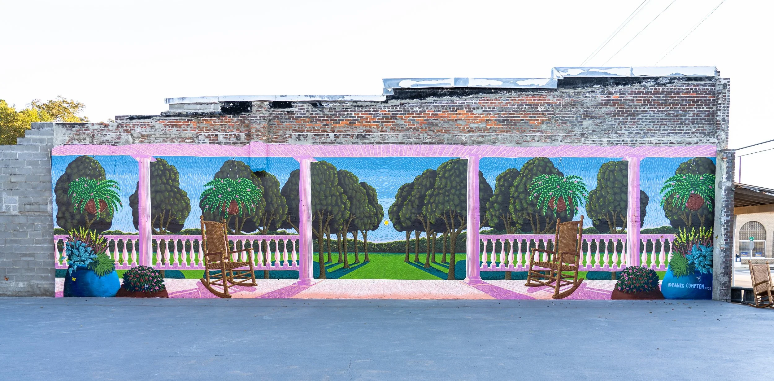 Site-specific mural in Linden, Alabama, depicting a Southern porch with rocking chairs, trees, flowers, and a garden landscape.