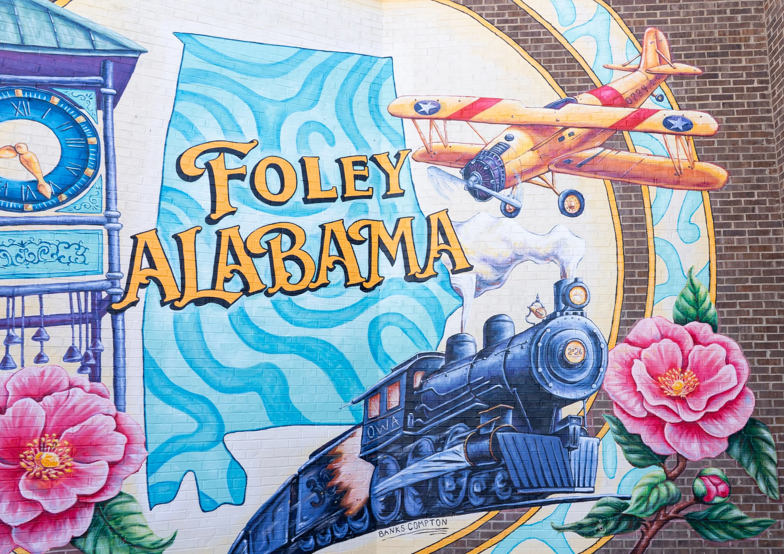Foley Photo Mural by Banks Compton at Downtown OWA featuring Foley Alabama lettering, a historic train, N3N biplane, and camellias.