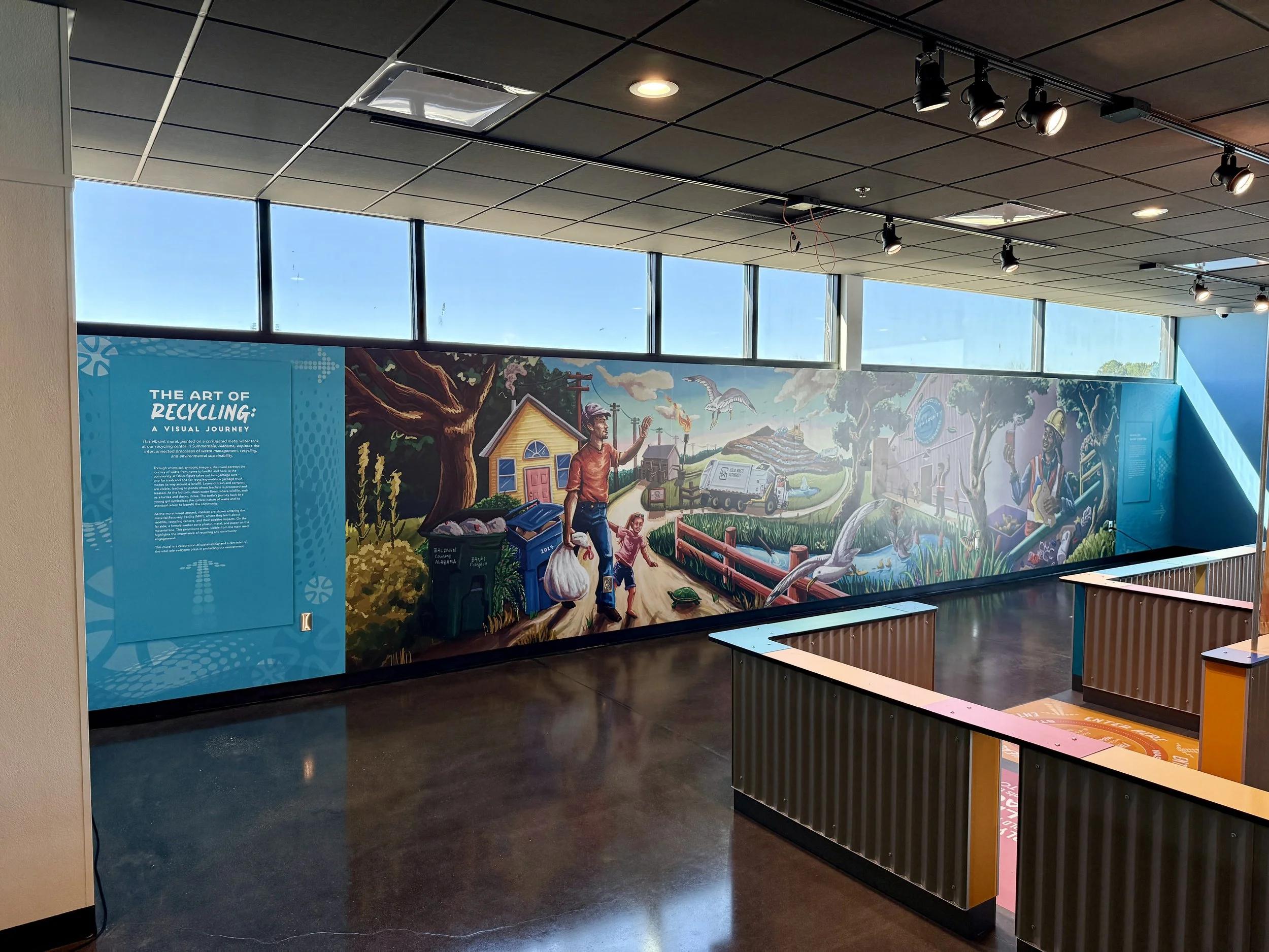 A mural illustrating community recycling efforts, featuring people recycling, a tree, a house, a trash truck, and environmental themes at an indoor public space.
