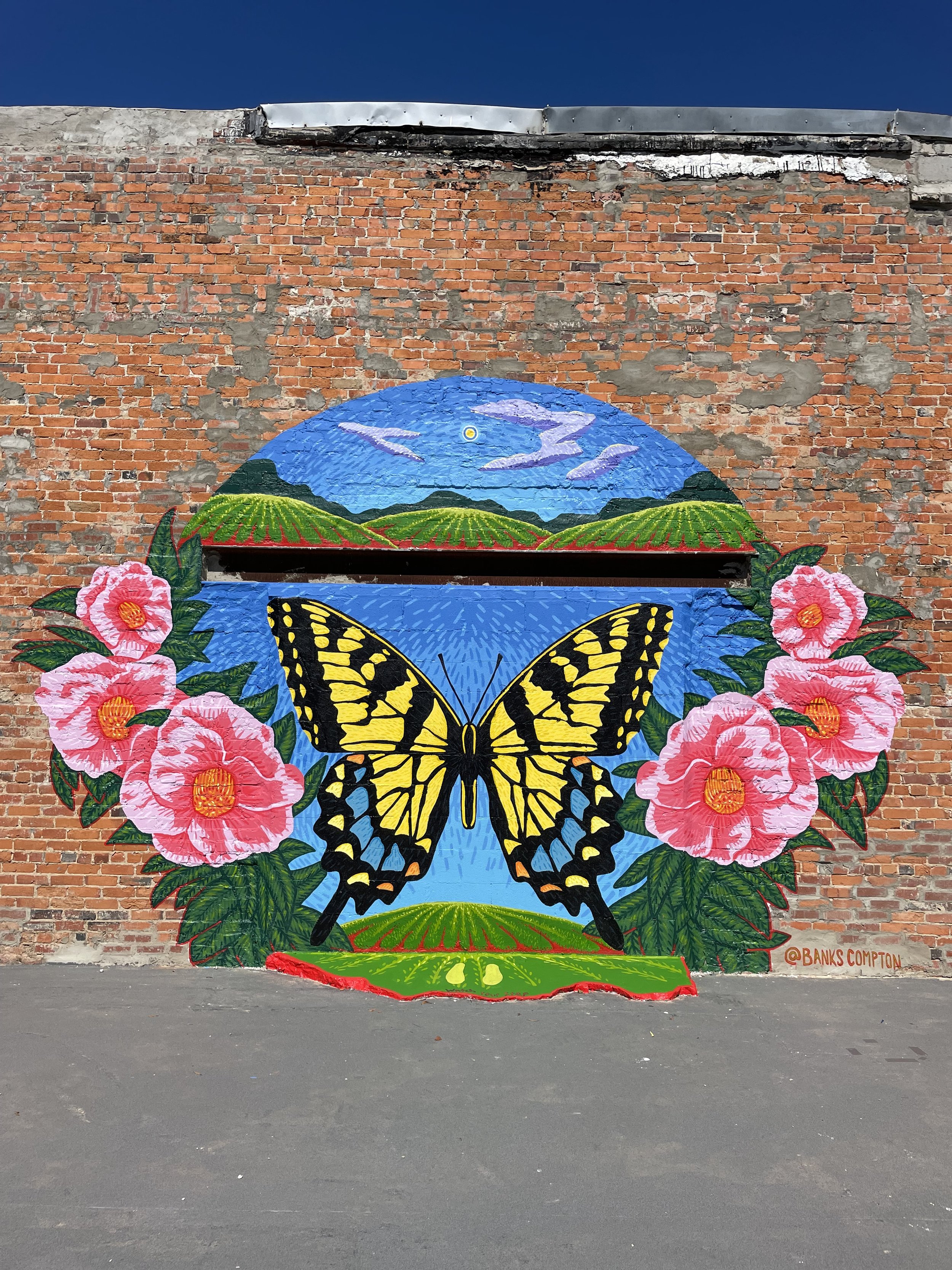 Eastern tiger swallowtail butterfly mural by Banks Compton in downtown Linden, Alabama, surrounded by camellias and a rural landscape.