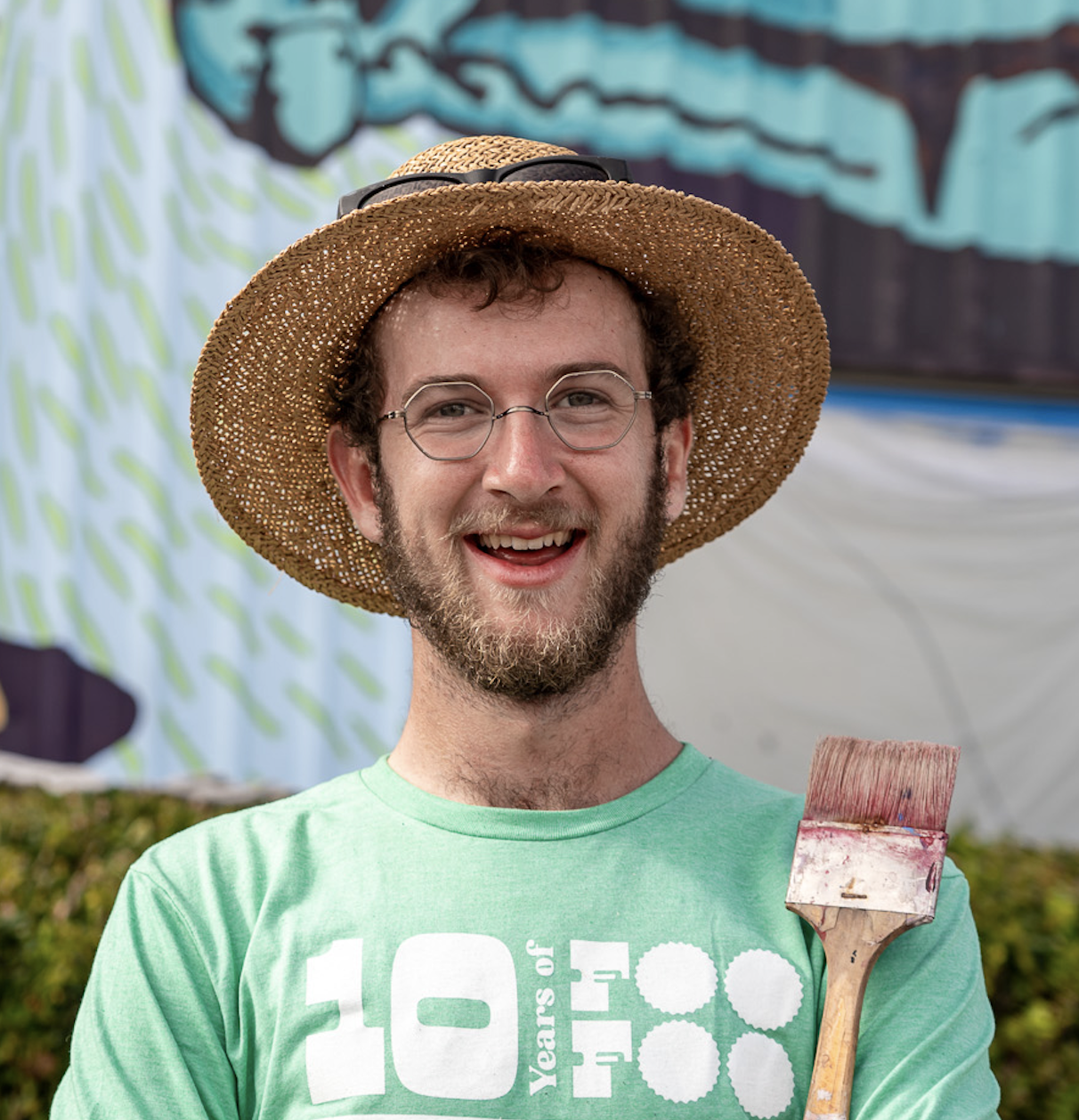Alabama mural artist Banks Compton holding a paintbrush in front of one of his colorful murals.
