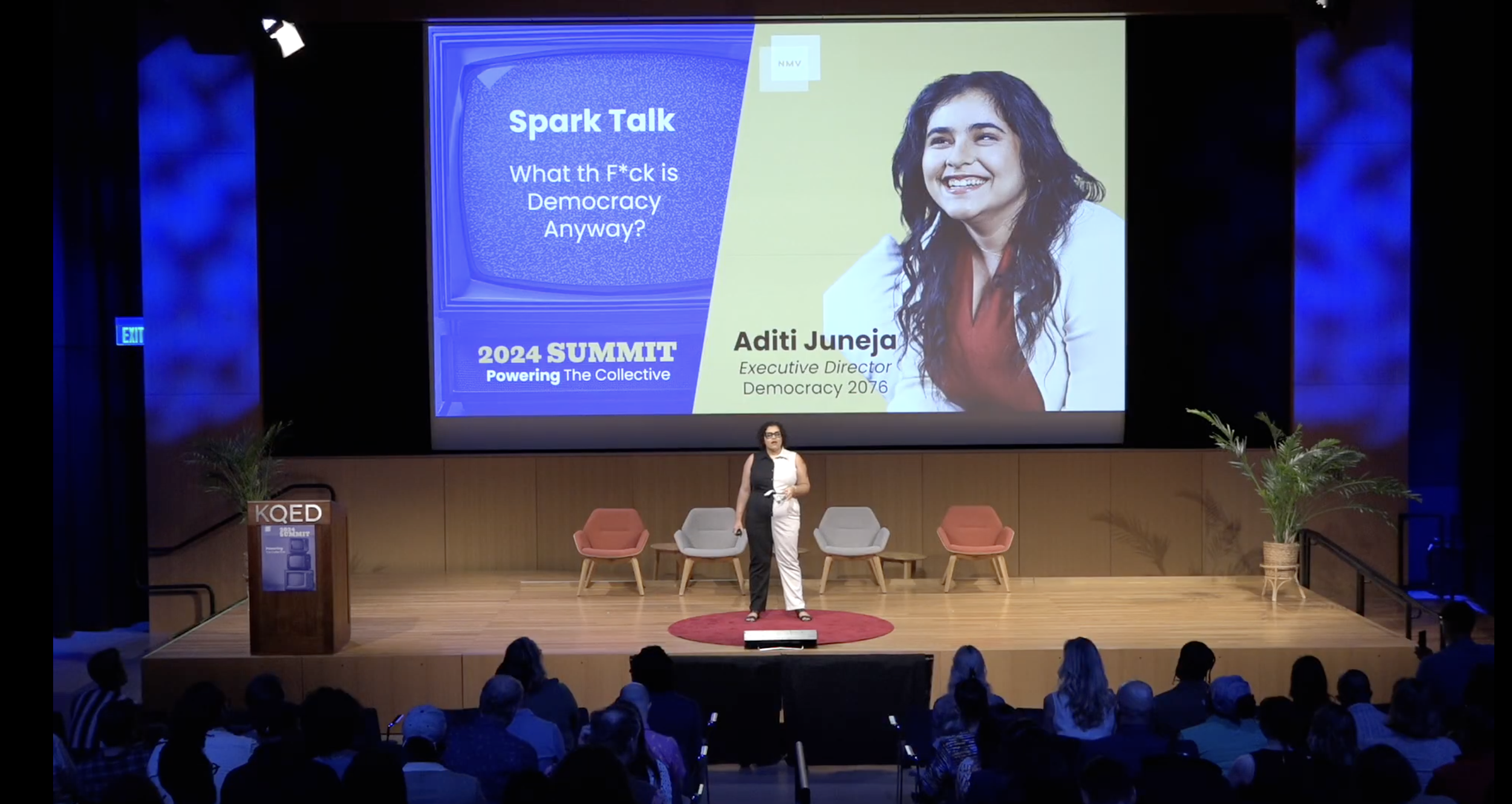 Aditi Juneja stands on stage in front of a large screen, presenting in front of an audience.