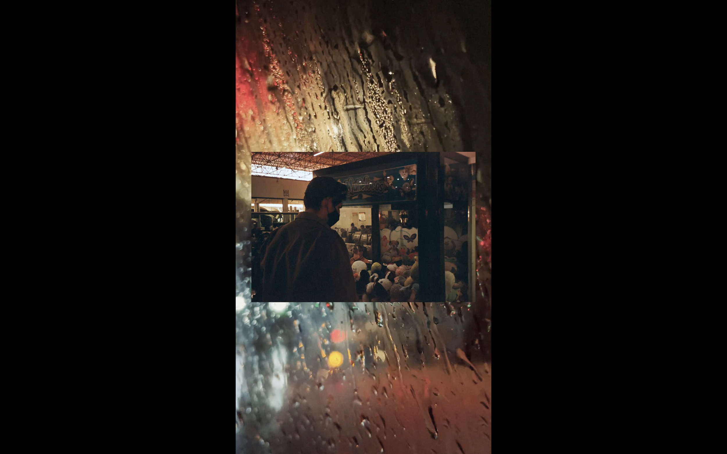 art video by swiss artist SEVERIN HALLAUER - consisting  of analog photographs and videos.  Rain streaked window with blurred city lights, showing a person and a claw machine inside a dimly lit arcade or amusement area.