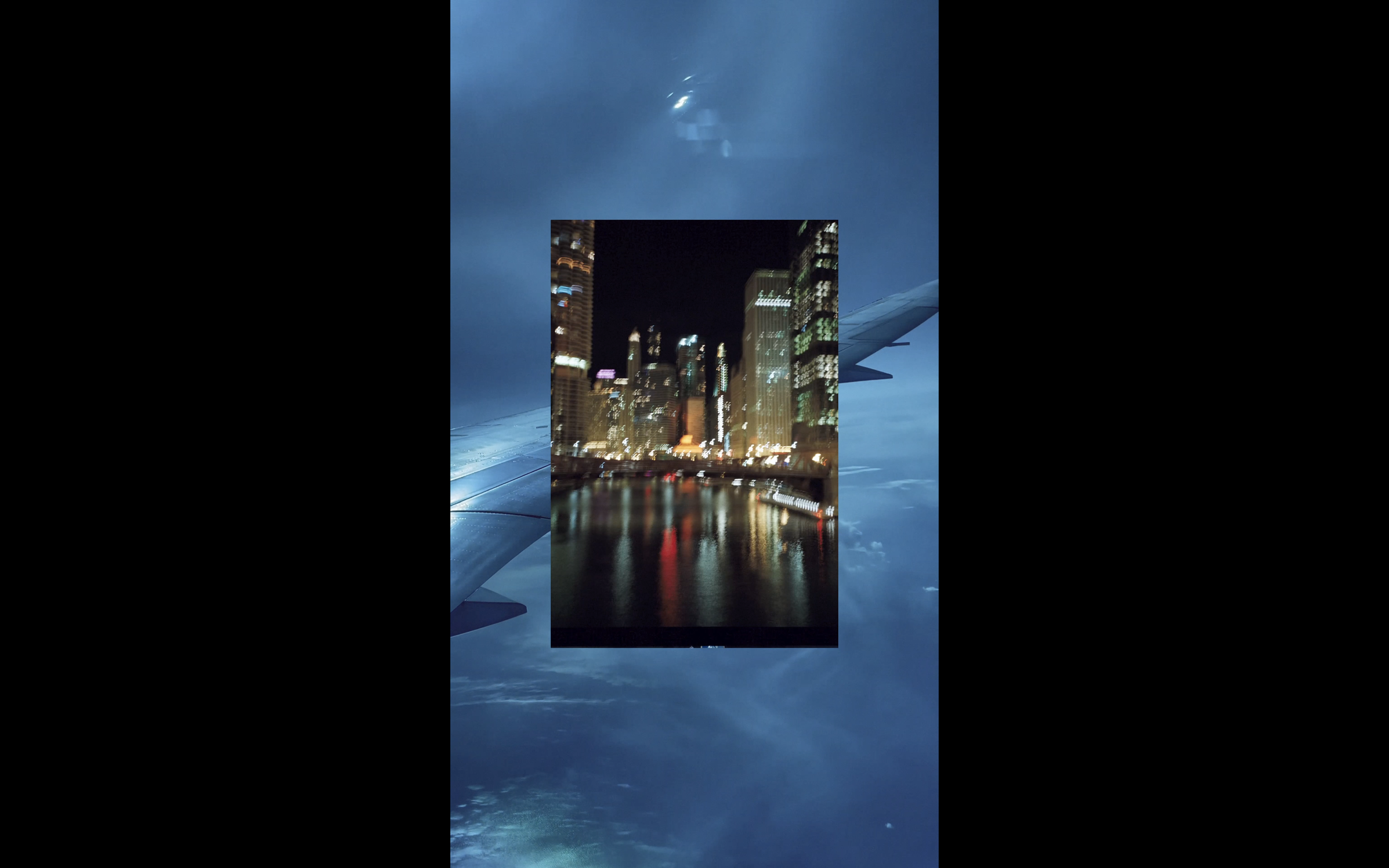 art video by SEVERIN HALLAUER - consisting  of analog photographs and videos. Nighttime city skyline with illuminated buildings and reflections on the water, seen from an airplane window. 