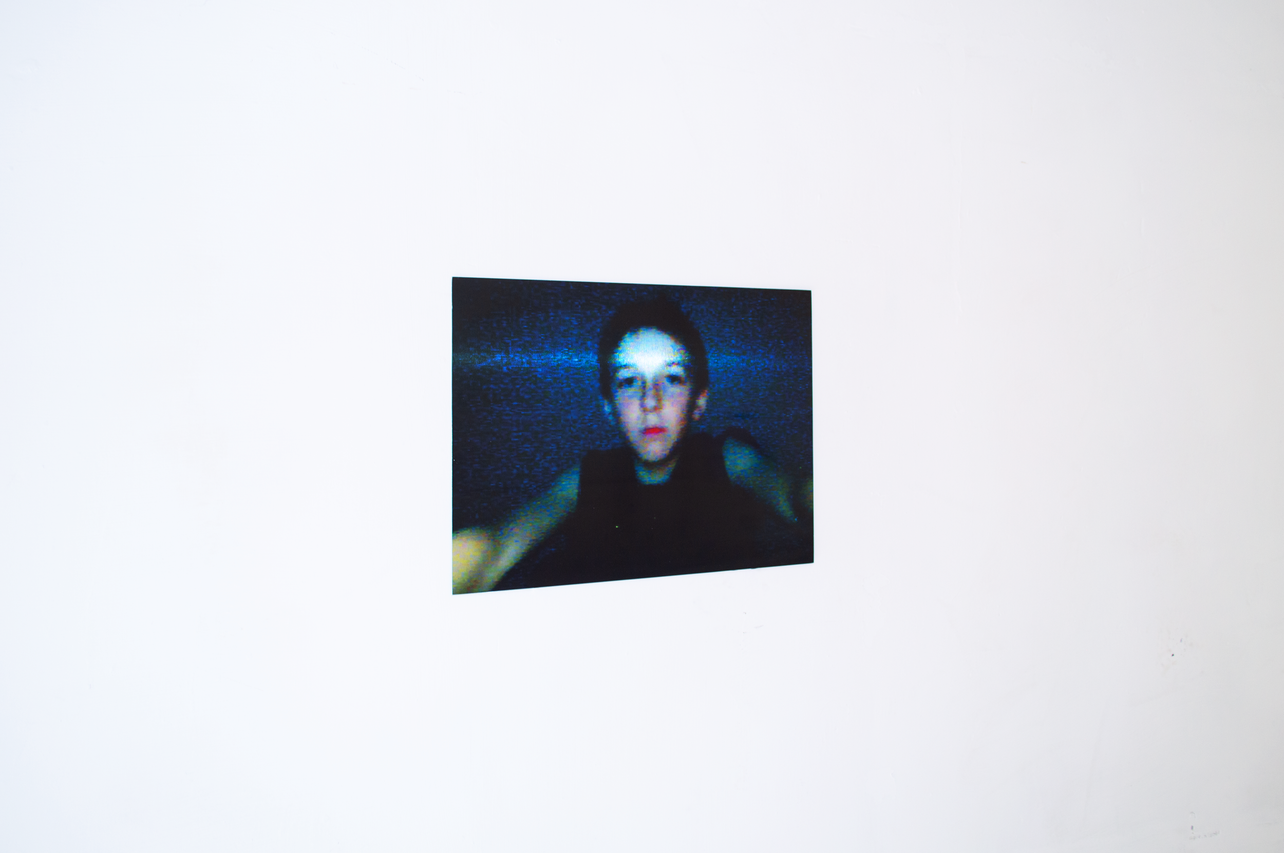 First Selfie by SEVERIN HALLAUER. A framed photo of a young boy with short hair and a serious expression, mounted on a white textured wall.