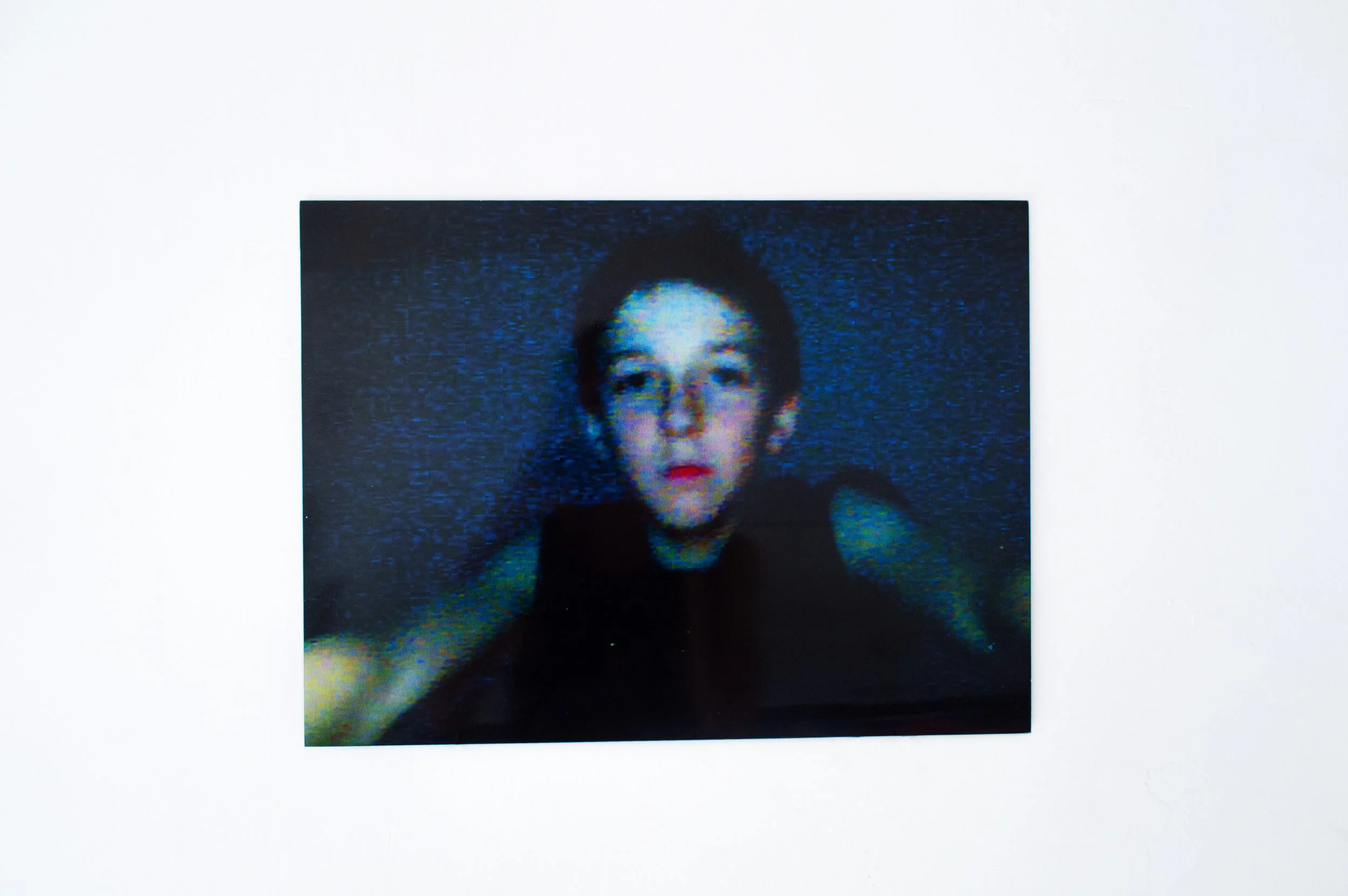 First Selfie by SEVERIN HALLAUER. A framed photo of a young boy with short hair and a serious expression, mounted on a white textured wall.