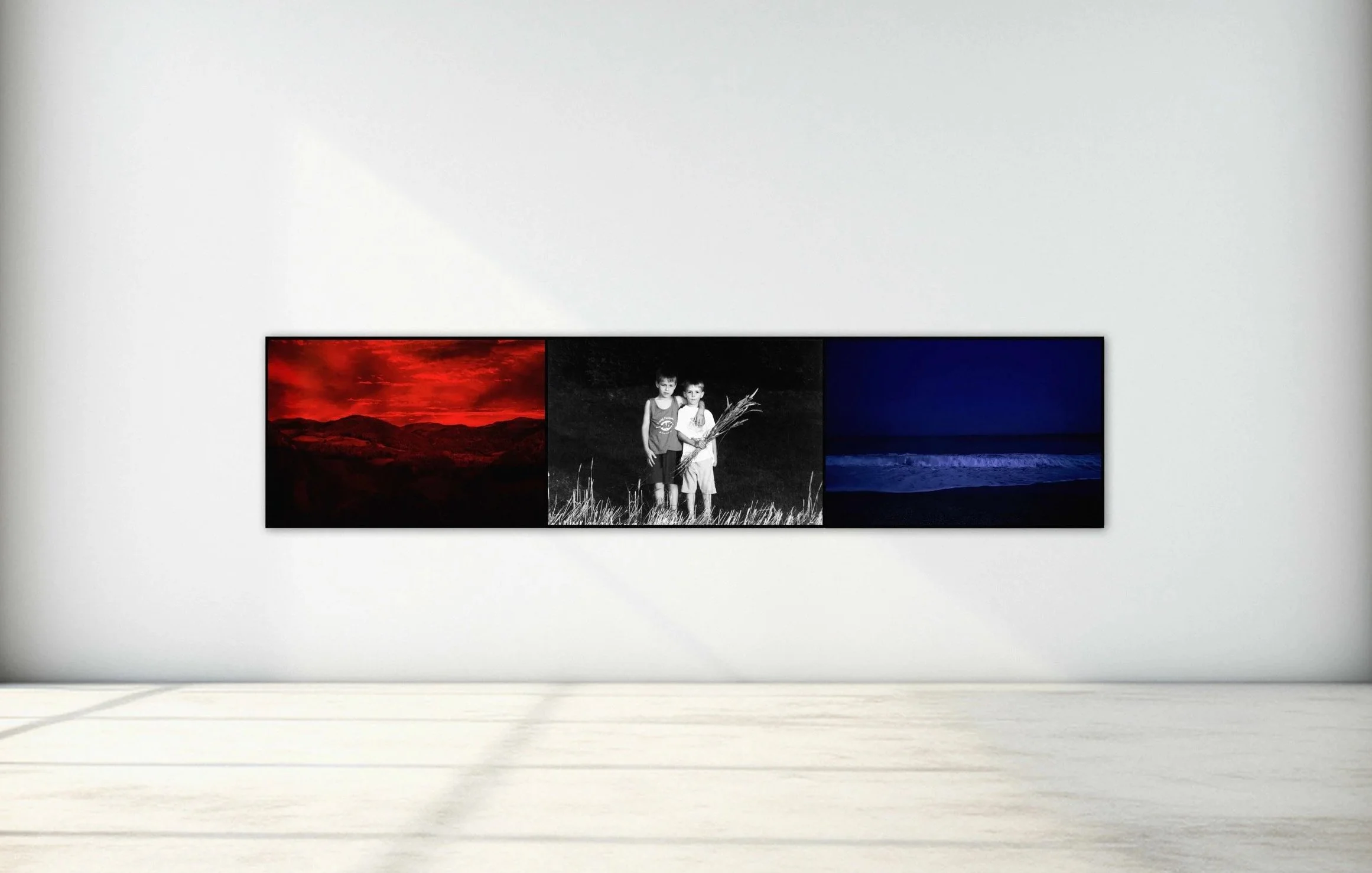 Triptych of three photographs on a white gallery wall: a red-toned landscape, two children in black and white, and an ocean scene at night.