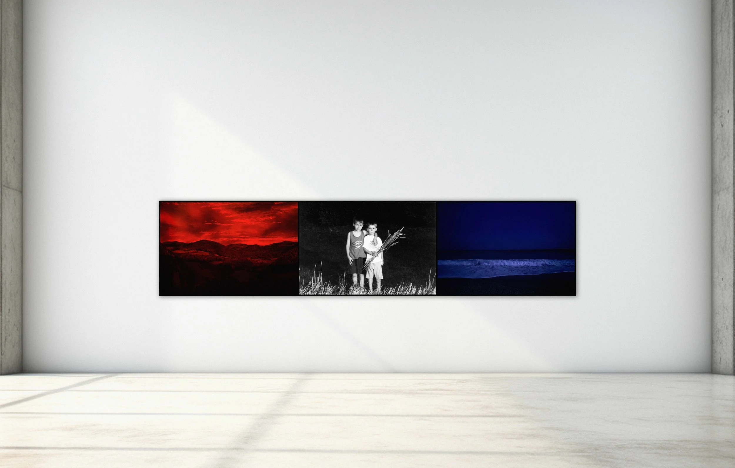 Triptych of three photographs on a white gallery wall: a red-toned landscape, two children in black and white, and an ocean scene at night.