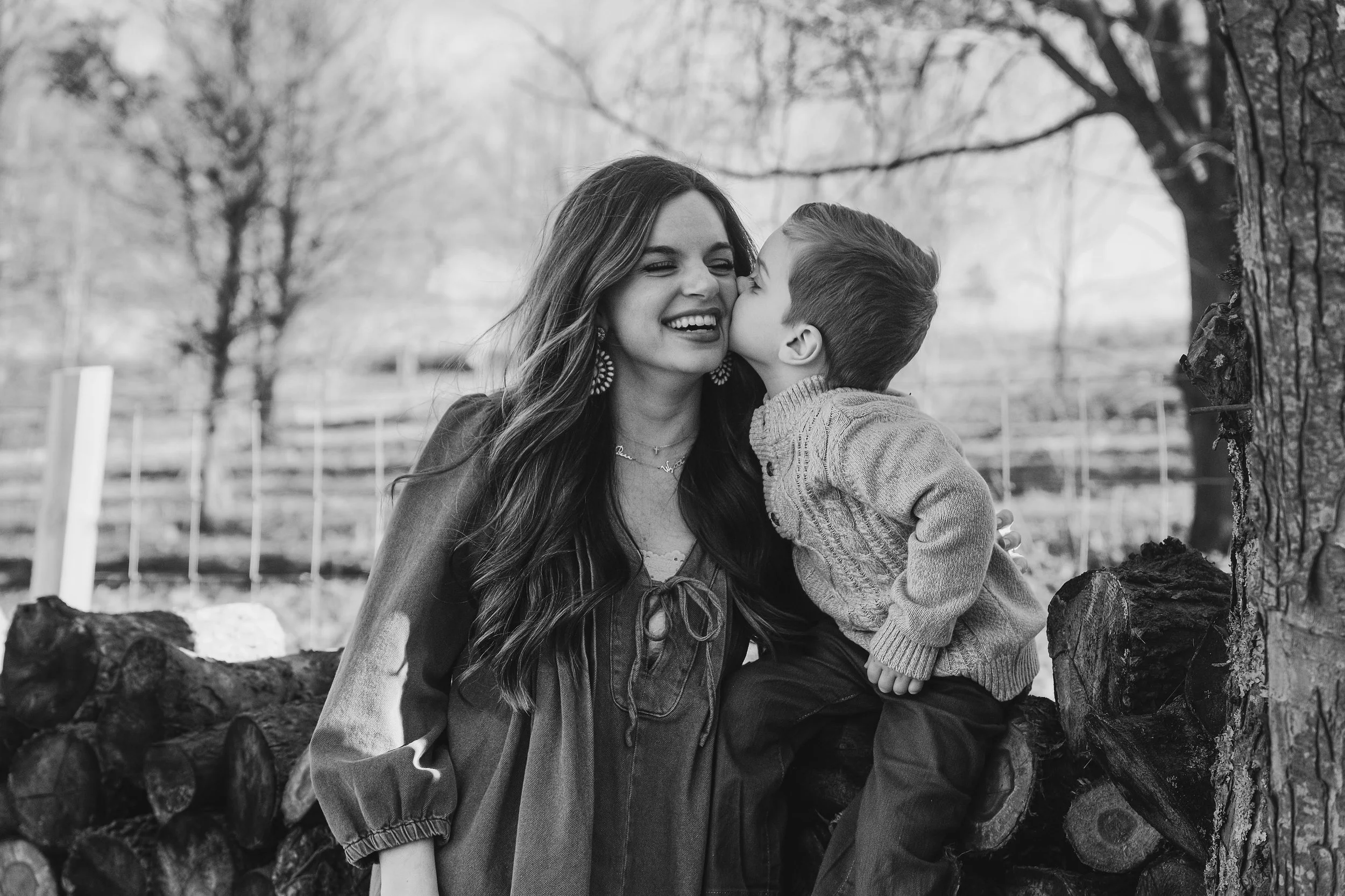 A woman with long hair and a young boy kissed on the cheek outdoors in black and white.