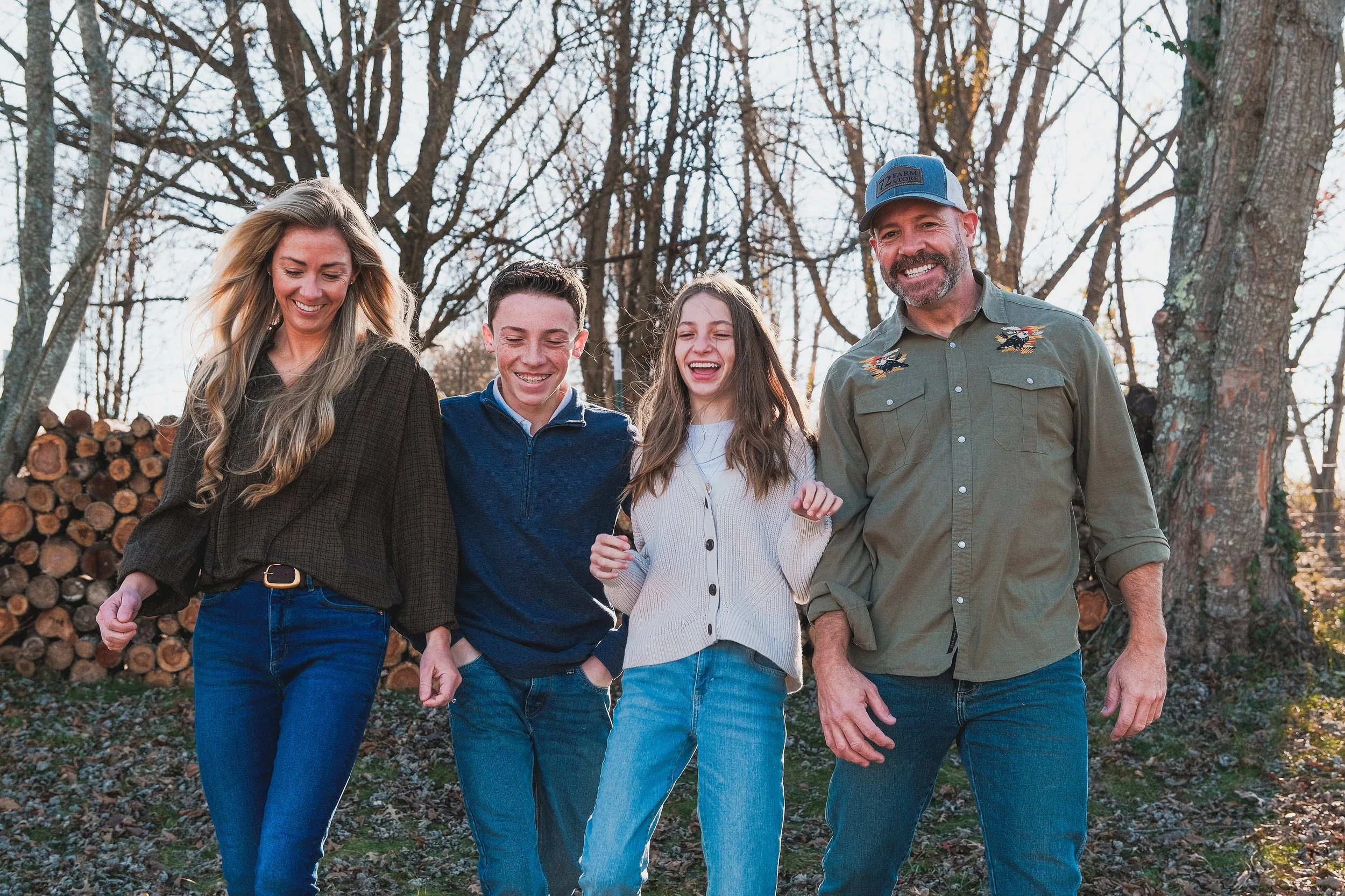 A family of four walking outdoors through wooded area, smiling and laughing together during daytime.