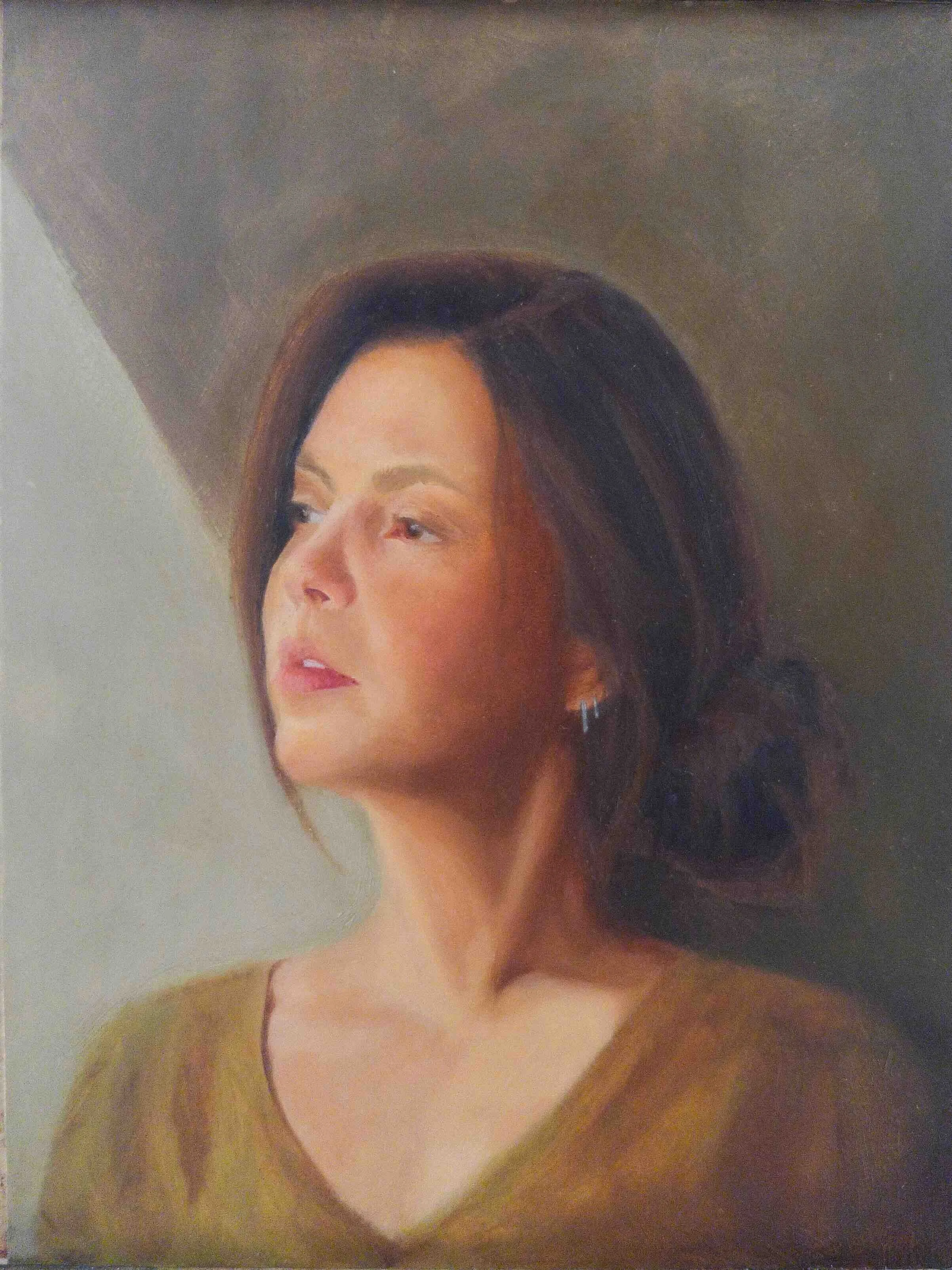 A portrait of a woman with dark brown hair styled in loose waves. She has light skin and is wearing a earrings. The background is a plain light-colored wall.