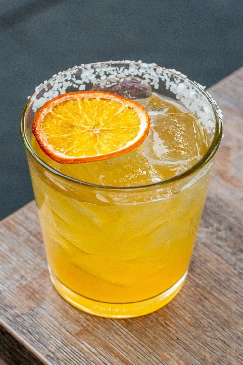 A glass of orange juice with ice, garnished with a slice of dried orange, on a wooden surface.