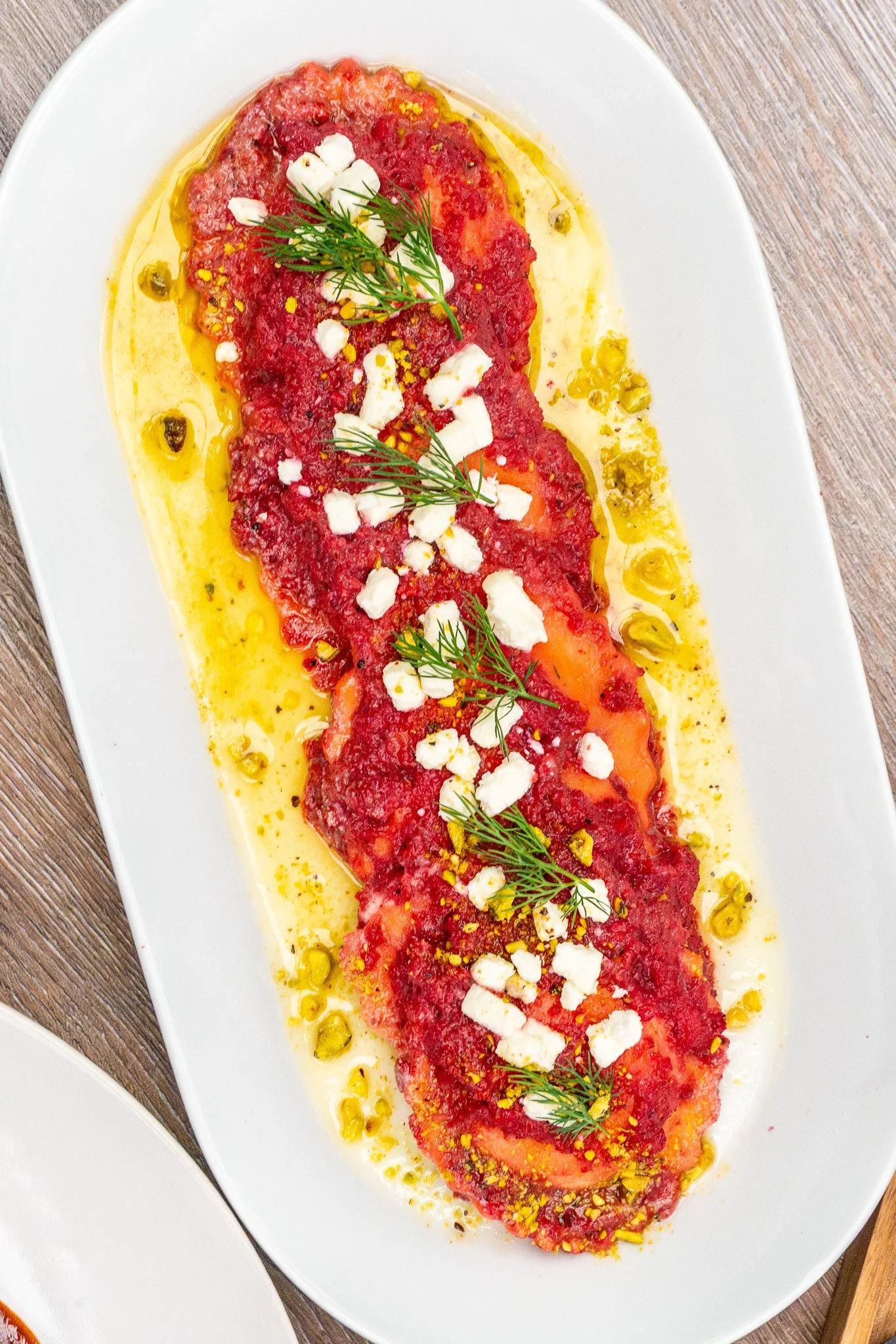 Sliced tomatoes topped with crumbled cheese, fresh dill, and drizzled with oil on a white platter.