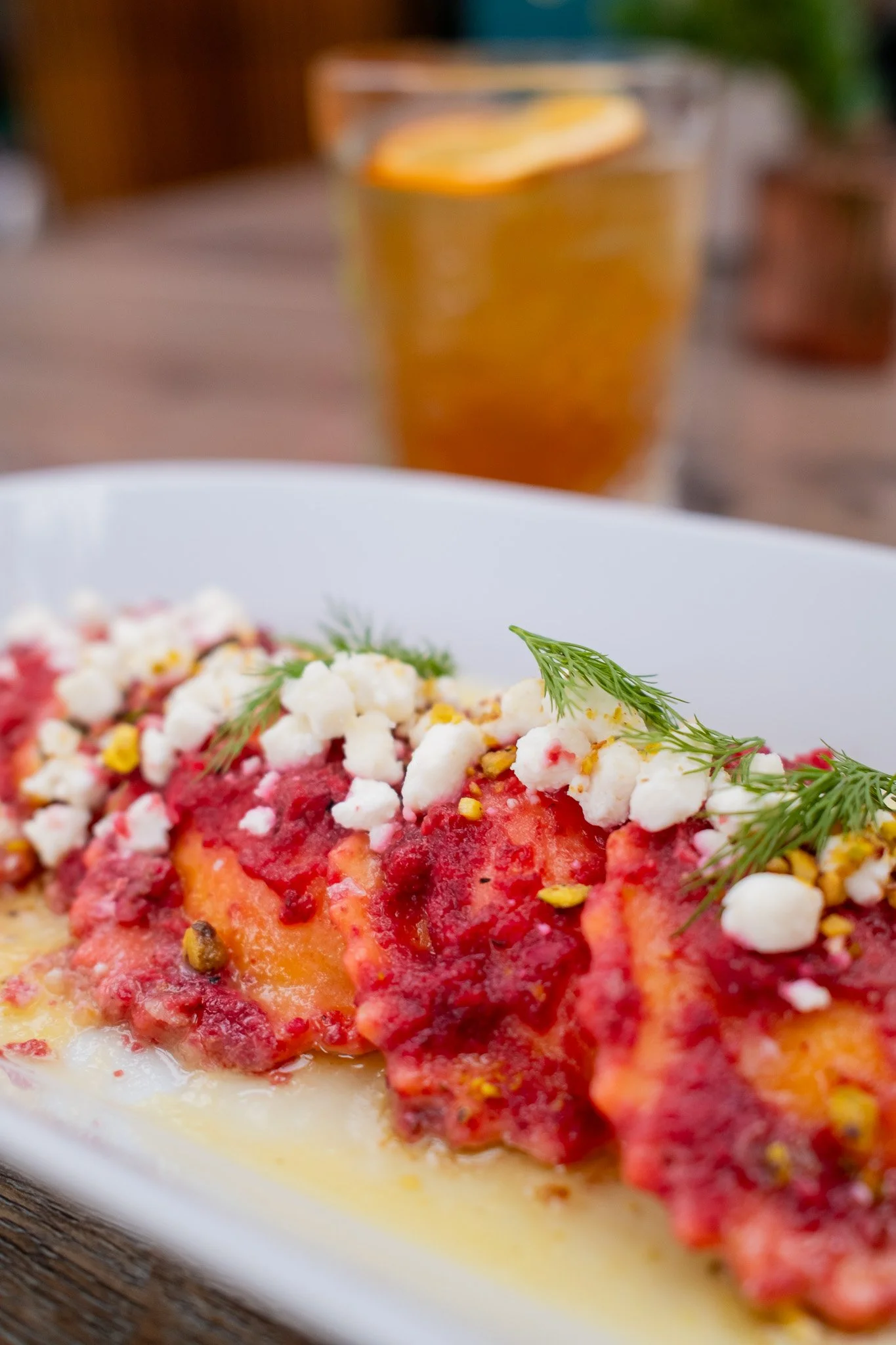 Close-up of a plate of lasagna garnished with herbs and cheese, with a glass of iced tea with a lemon wedge in the background.