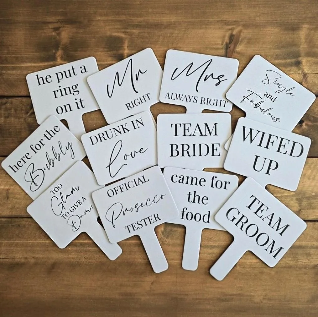 Collection of wedding-themed cards with humorous and descriptive phrases, including titles like 'Mr RIGHT,' 'Mrs ALWAYS RIGHT,' 'Single and Fabulous,' 'WifeD UP,' and other wedding role and personality descriptions, arranged on a wooden surface.