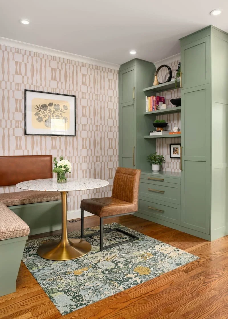interior designed dining area with a green built in cabinet, tan seating, and gold elements in an updated midcentury modern style. A framed photo of flowers is hung on a white and gold patterned wallpapered wall.