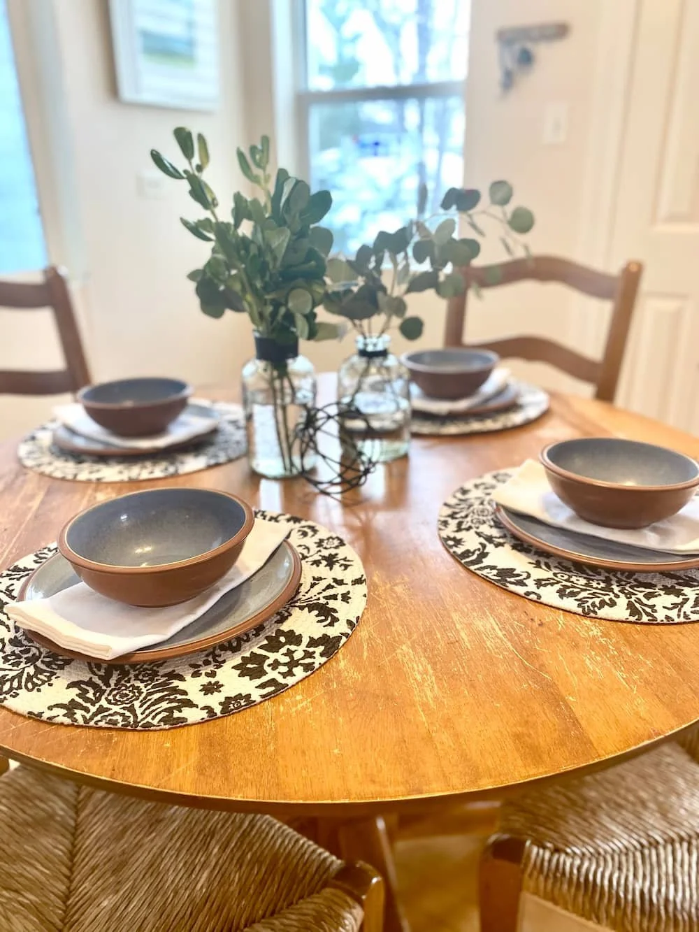 home staged place settings of bowls and plates on patterned placemats with a green plant centerpiece