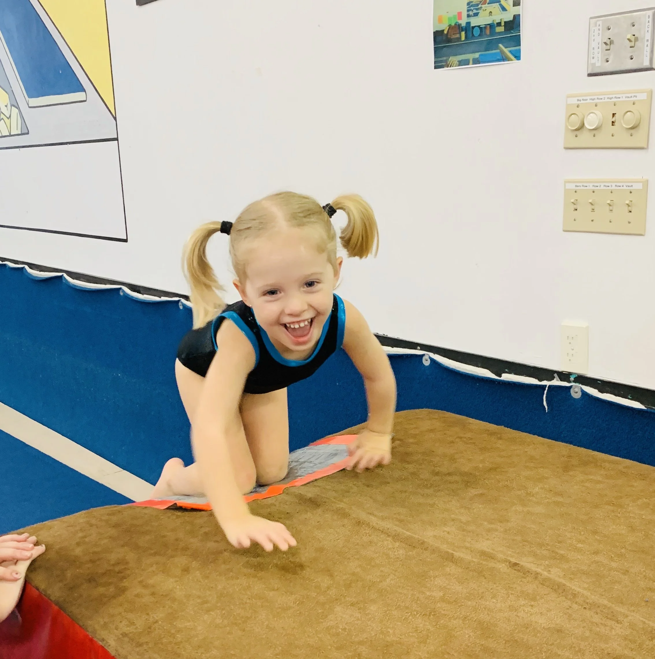 A young girl with blonde hair in pigtails crawling on a gymnastics mat.