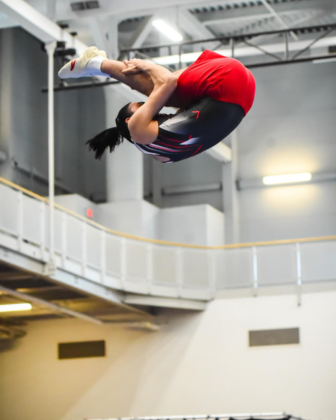 Man in black and red trampoline uniform performing a flip in a pike position
