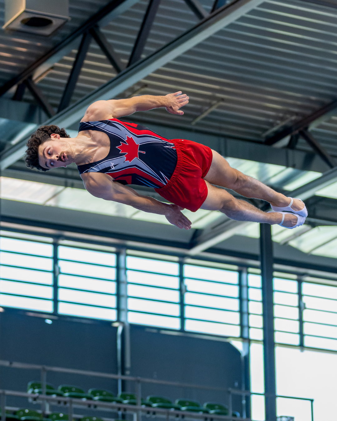 Man in team canada trampoline uniform is horizontal performing a flip in a straight body position