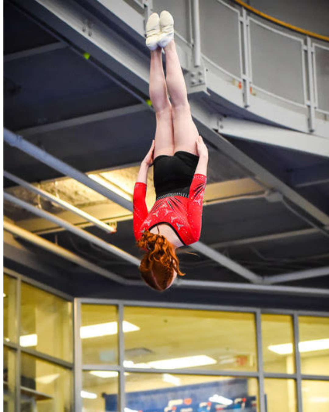 Girls in black and red trampoline uniform performing a flip in a straight body position