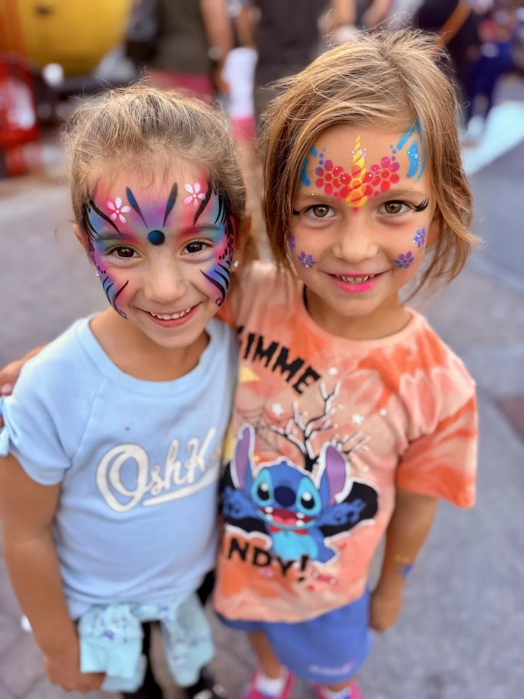 Two girls smiling with their faces painted in bright colours