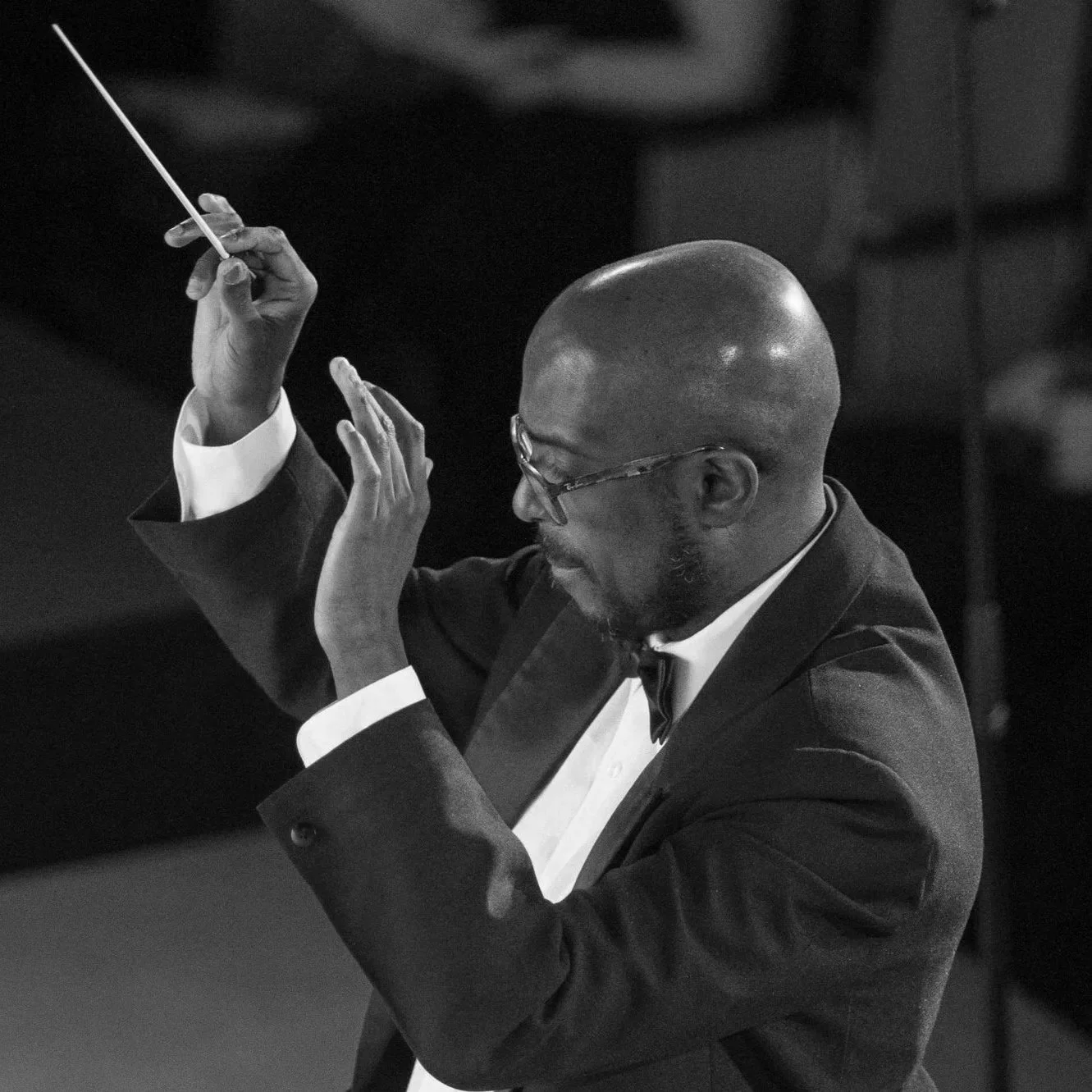 Image of person wearing a tuxedo, with a baton, conducting