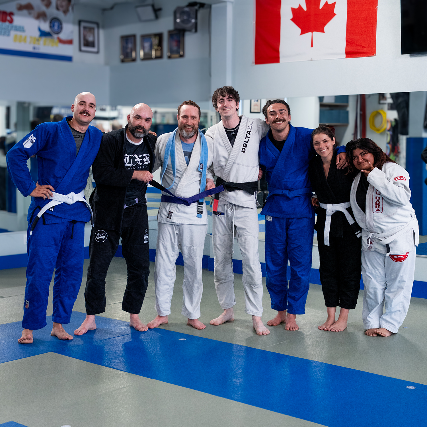 Two people practicing Brazilian jiu-jitsu on mats, with the person in a black gi executing a grappling move and smiling.