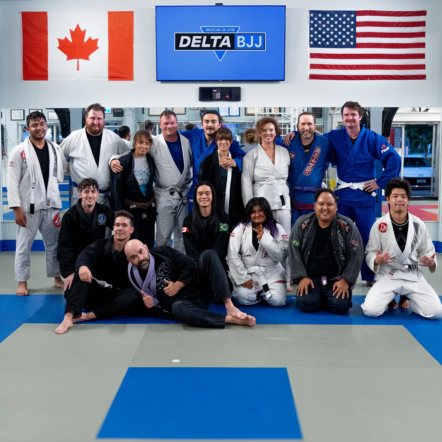 Two people practicing Brazilian jiu-jitsu on mats, with the person in a black gi executing a grappling move and smiling.